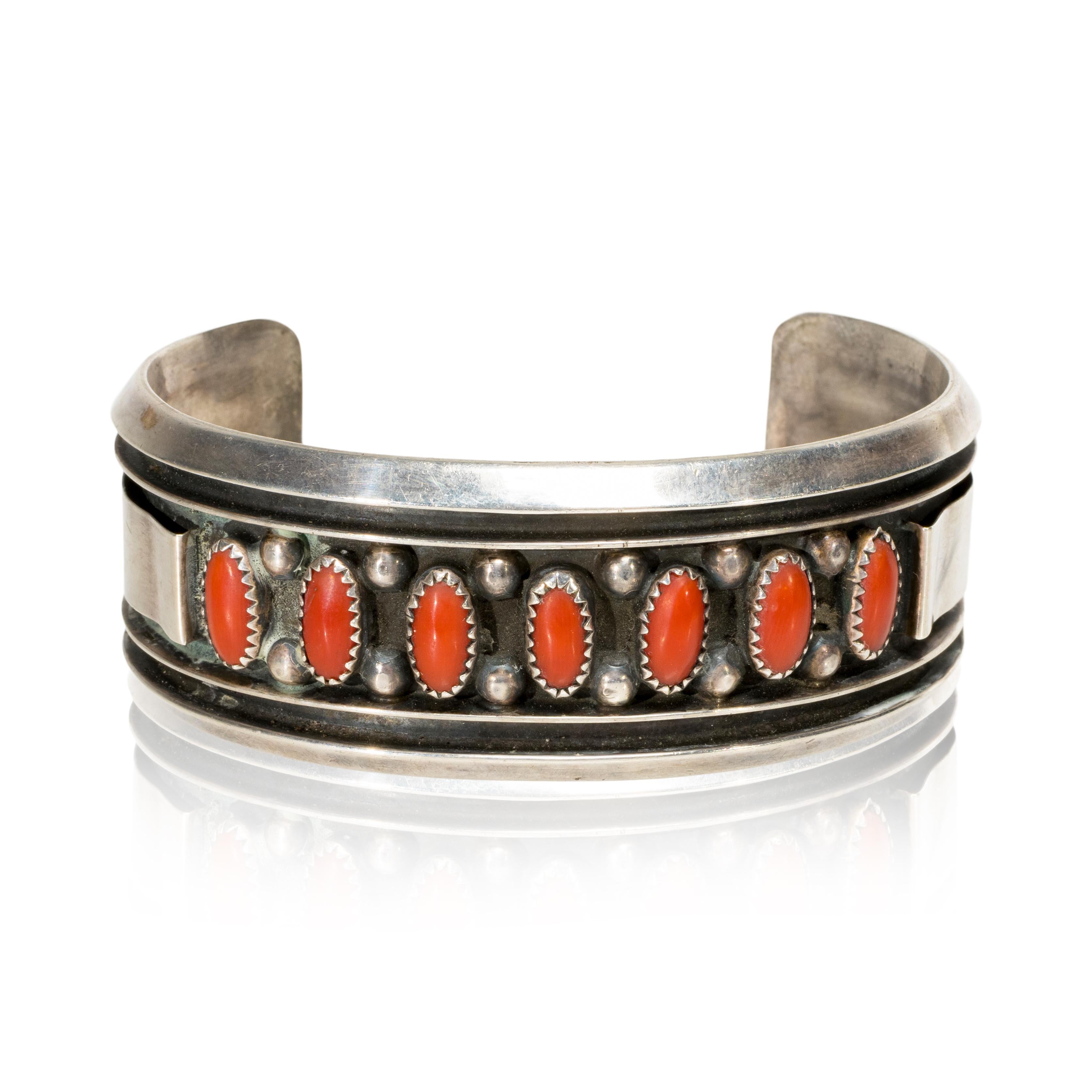 Navajo sterling and coral cuff bracelet. Signed J. S. Jackie Singer, Navajo. Seven recessed bezel set red coral cabochons with beaded accents in shadow box frame.

PERIOD: Late 20th Century
ORIGIN: Southwest - Navajo, Native American
SIZE: 5 1/2