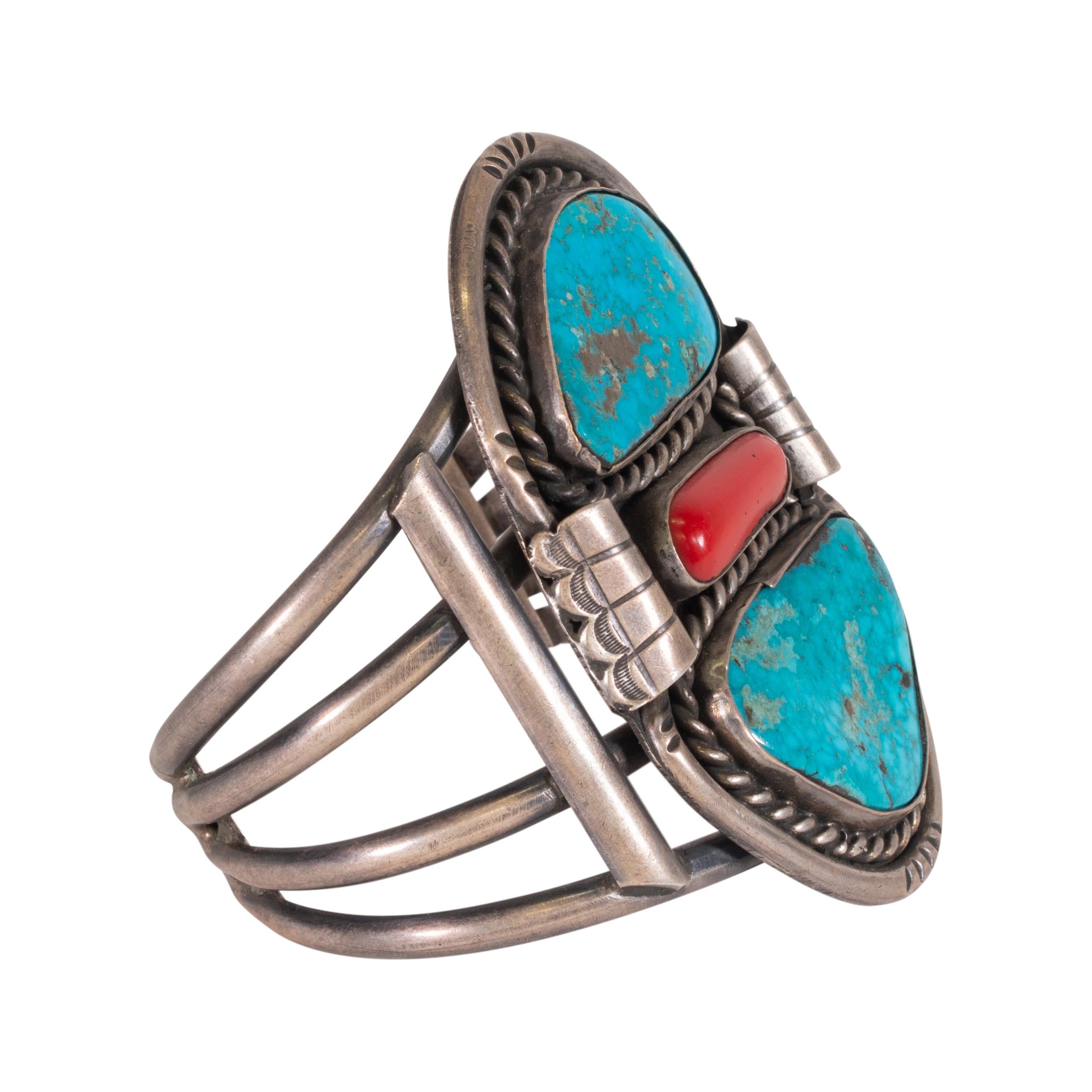Navajo Manschettenarmband mit zwei Türkissteinen und Korallen in der Mitte. Der Türkis stammt aus der Morenci-Mine in Arizona und zeichnet sich durch eine leuchtend blaue Farbe mit goldener Matrix aus. Steine umgeben von einem gedrehten Seil und