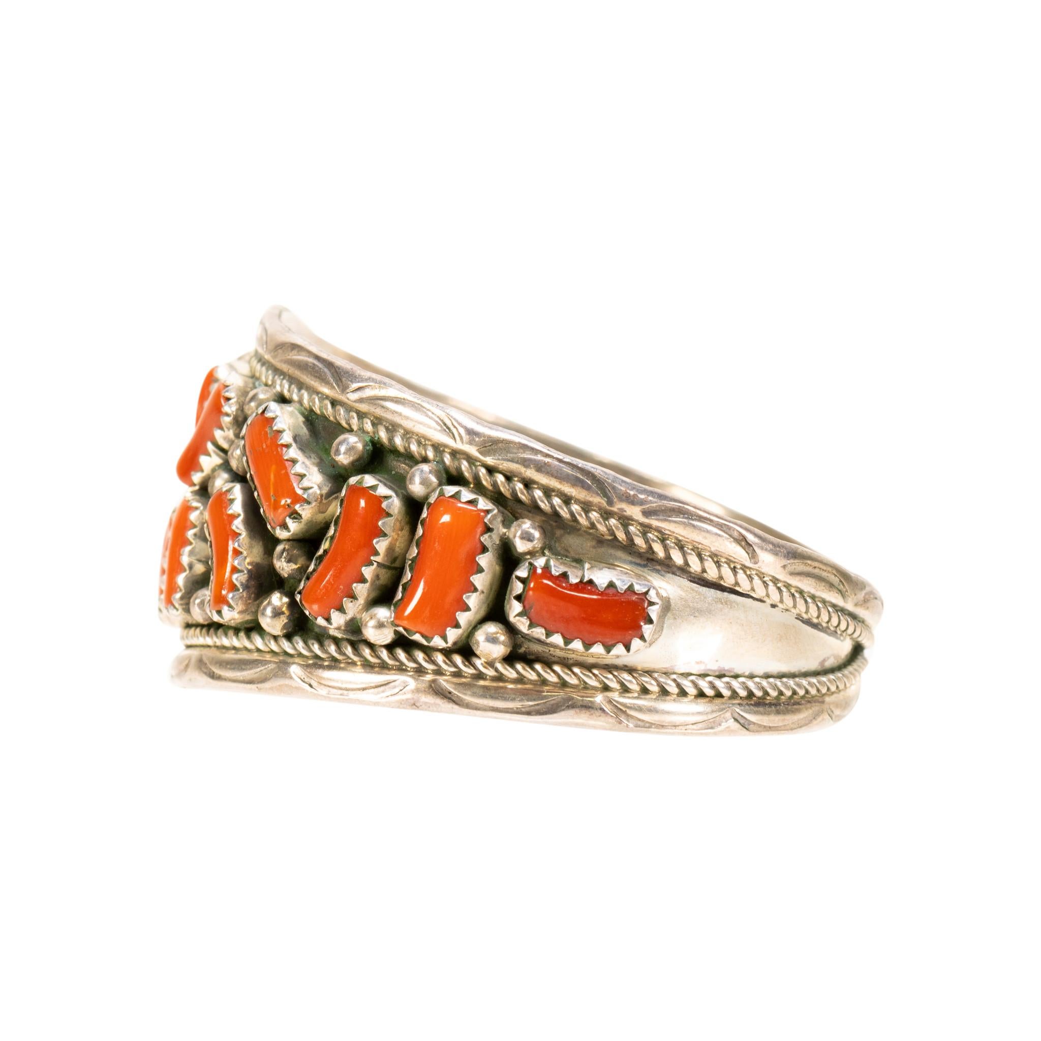 Bracciale Navajo in corallo e argento. Il braccialetto presenta 18 cabochon di corallo disposti in un motivo elettrico, ciascuno inserito in castoni d'argento a dente di sega con accenti di perline in argento. Disegni stampati a mano lungo i bordi e