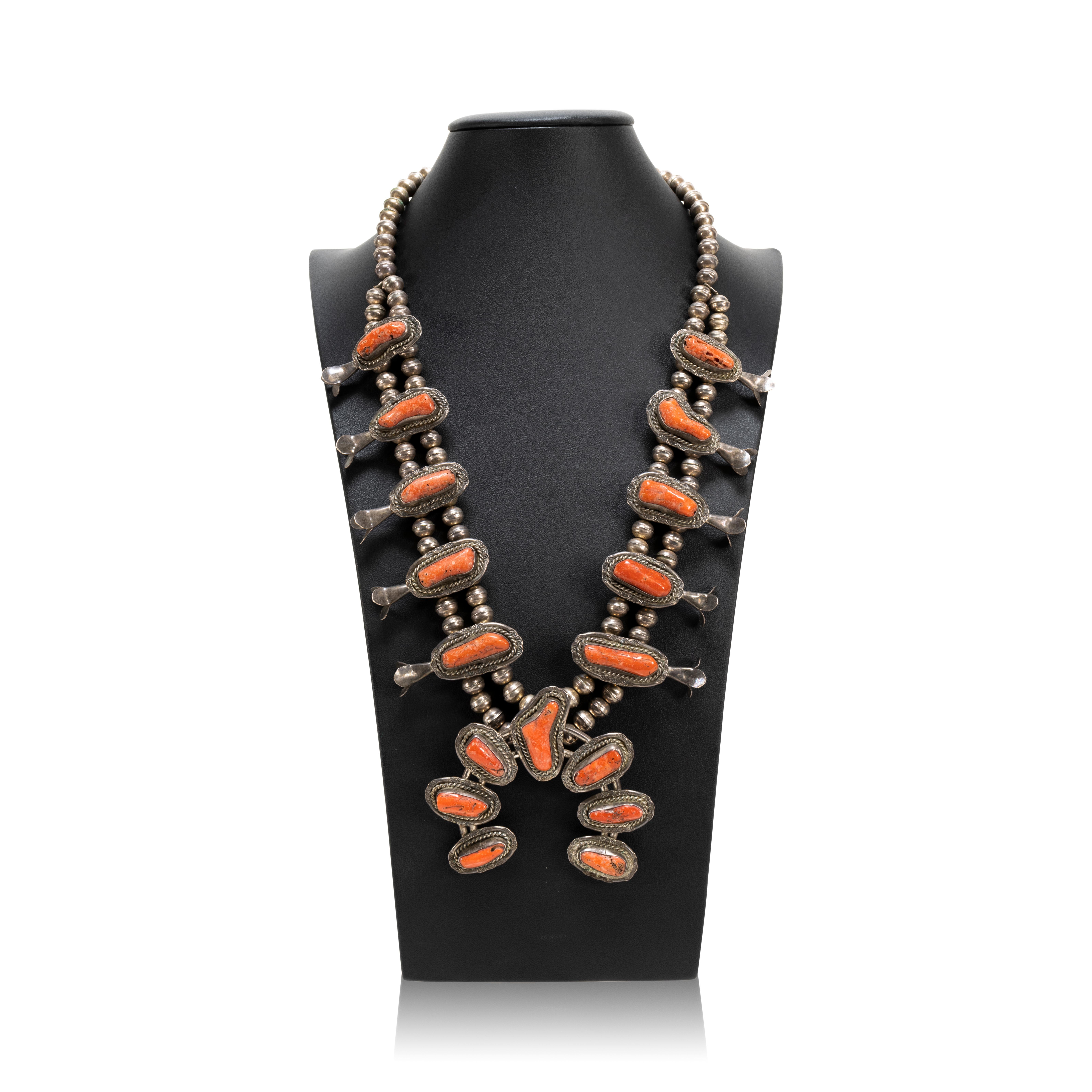 Navajo coral and sterling silver squash blossom necklace featuring a classic naja with seven beautiful coral cabochons accented by twisted rope and light hand stamped designs. The petal blossoms along the neck feature more stunning coral with the