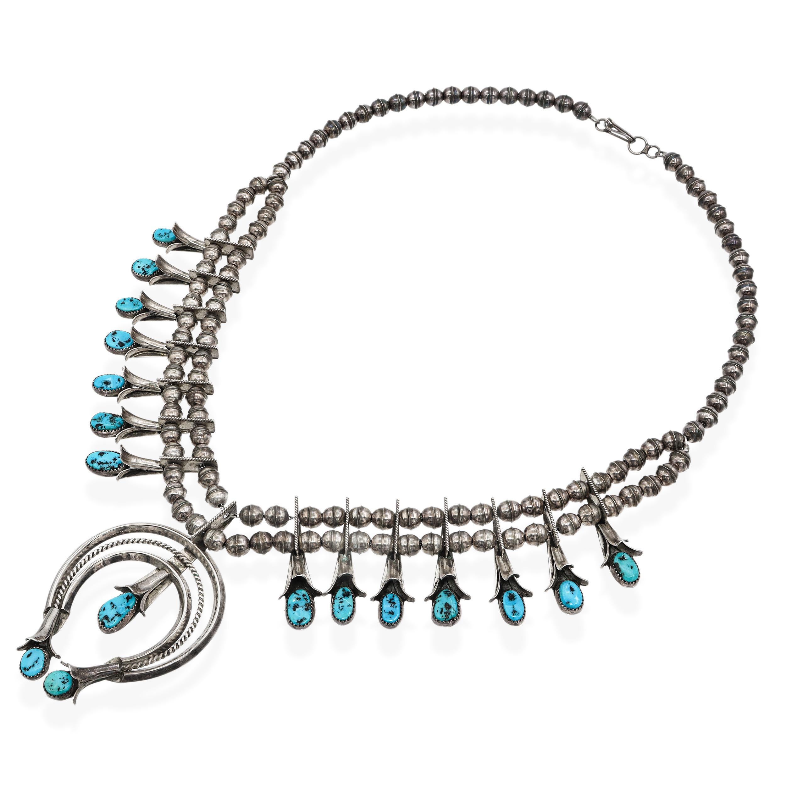 Questa eccezionale collana vintage di fiori di zucca Navajo mette in mostra l'arte tradizionale dei nativi americani, realizzata a mano in argento sterling e intarsiata con cabochon di turchese blu vivo. Ogni pietra è incastonata singolarmente,
