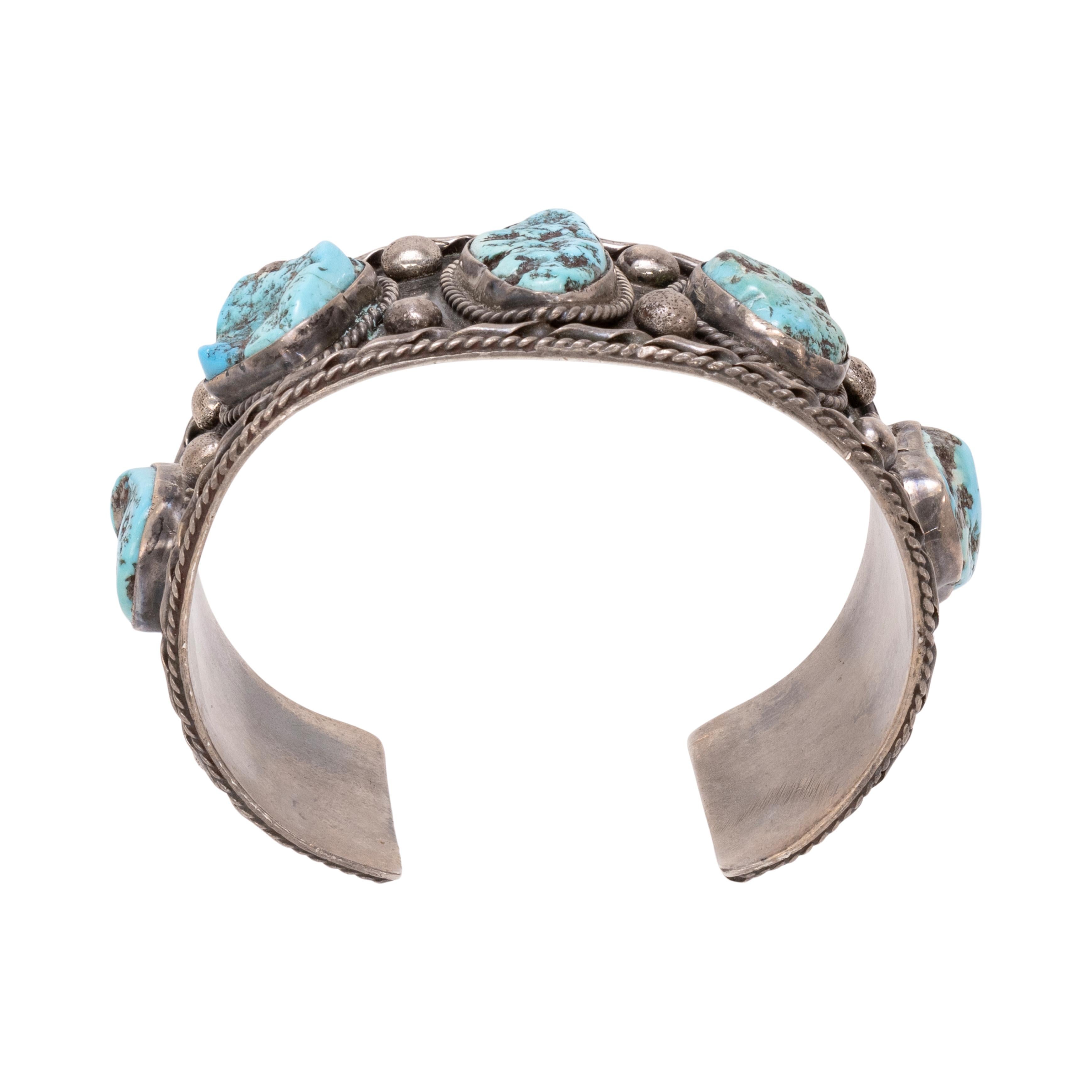 Bracciale Navajo a cinque pietre di turchese e argento sterling. Le pietre di turchese sono di un blu brillante con una pesante matrice marrone, da semilucide a grezze, incastonate in un castone con bordo in corda ritorta. Incastonato in un robusto