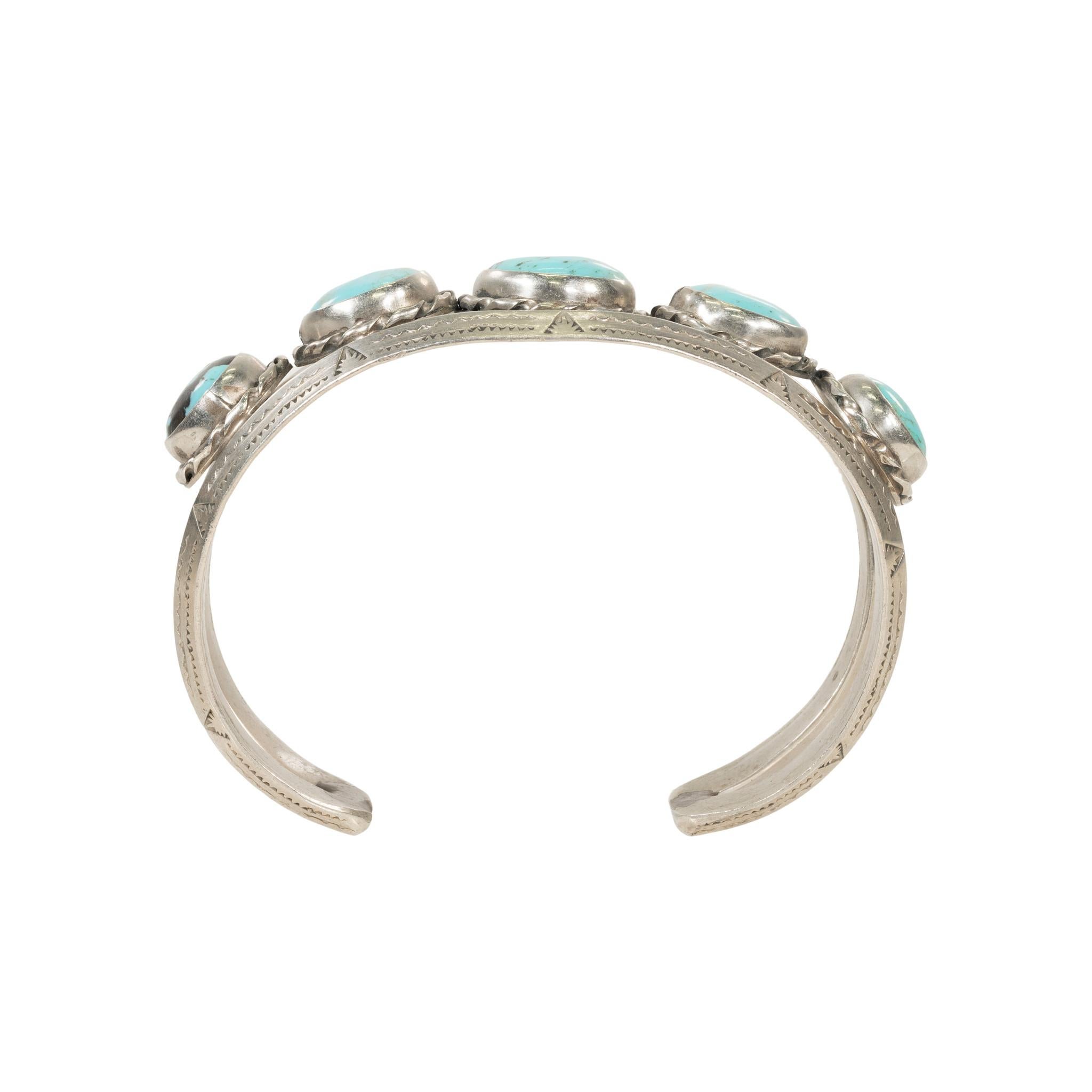 Bracciale Navajo a cinque pietre di turchese Kingman e argento sterling. Pietre rotonde con incastonatura a castone e bordo in corda tratteggiata. Le pietre sono di un bel blu acqua con matrice dorata e nera. Attaccato a un bracciale a doppia fascia