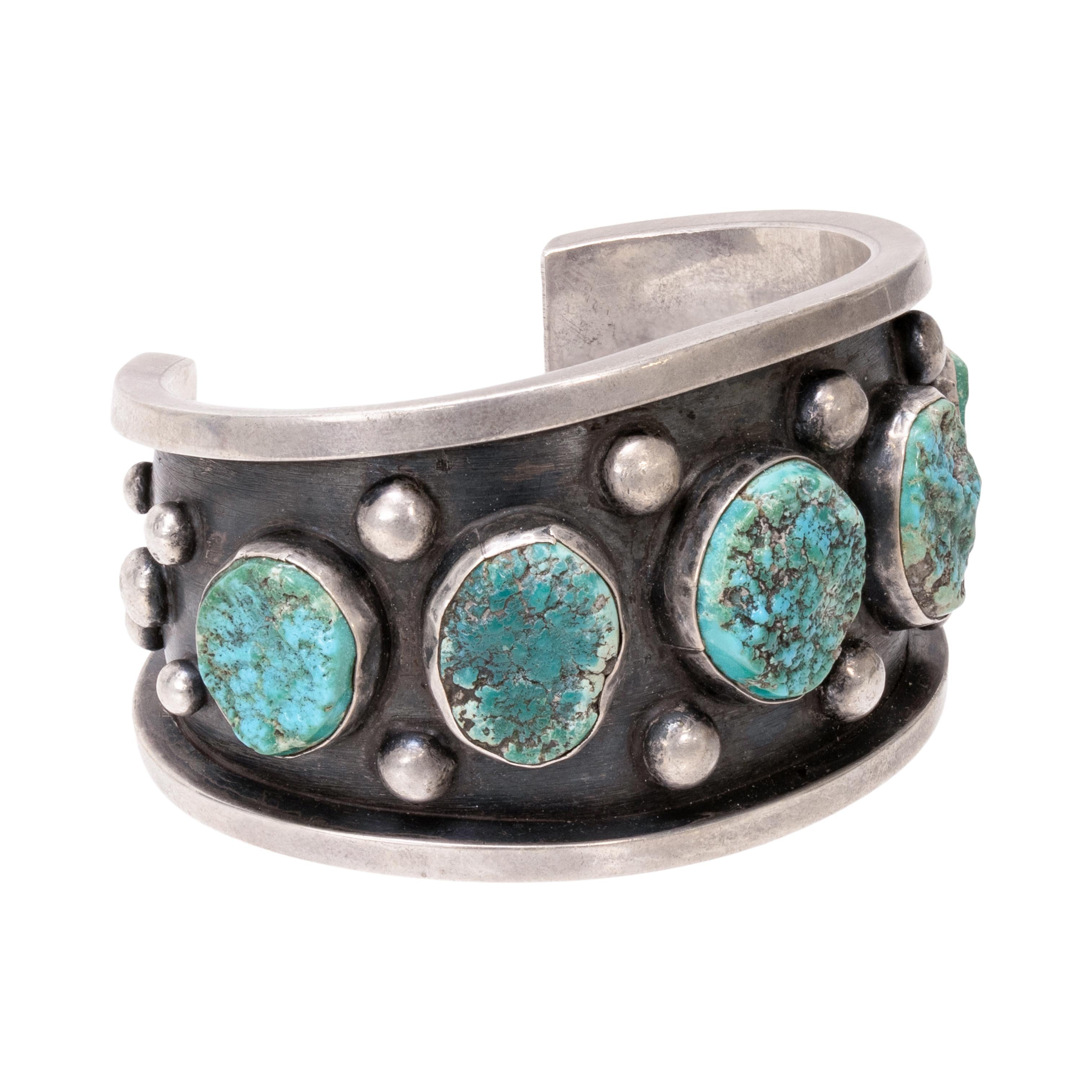 Bracelet manchette Navajo à cinq turquoises. Manchette en argent massif patiné, sertie d'un chaton et rehaussée de perles en argent. Les pierres sont d'un bleu profond semi-poli avec une matrice épaisse de couleur brune, noire et dorée. Pièce lourde