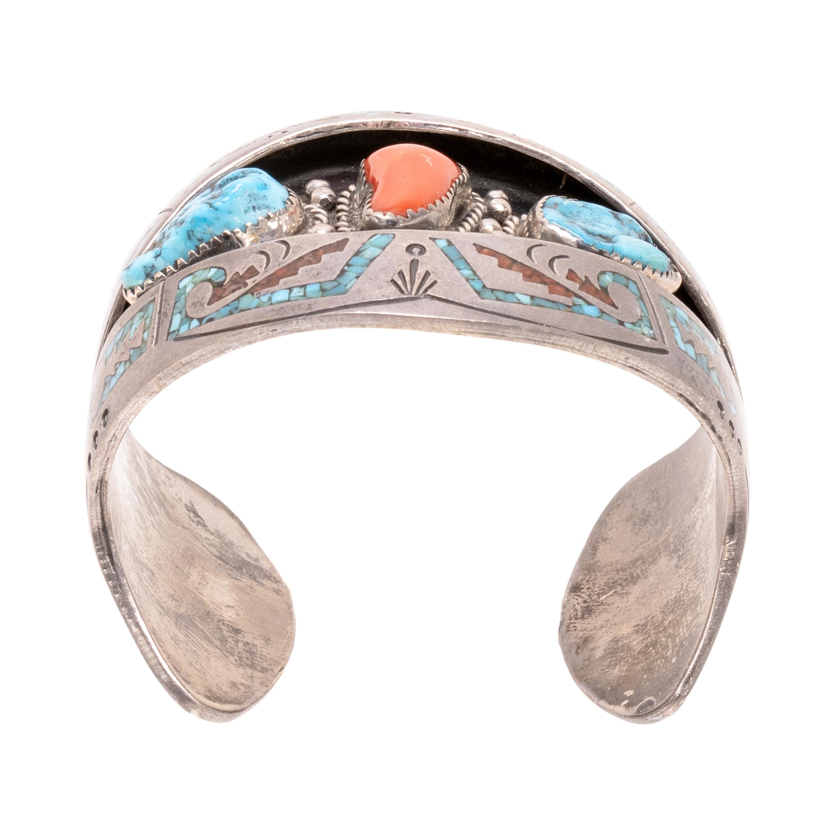Pulsera de incrustaciones navajo. Firmado B. James/HMIJ. Con centro de caja de sombra con una piedra de coral y dos piedras de turquesa Kingman rodeadas de bordes de cuerda retorcida y detalles de cuentas de ley. Enmarcada por una gruesa banda de