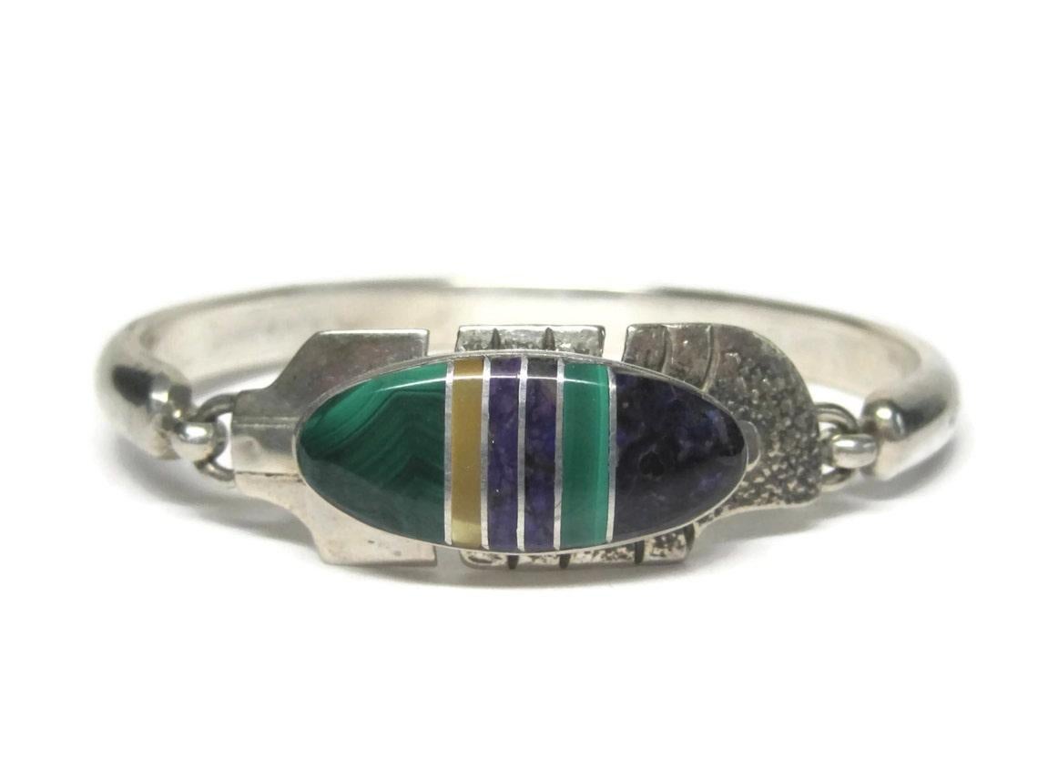 This gorgeous Navajo feather bracelet is sterling silver.

It features inlay in malachite, yellow mother of pearl, sugilite and charoite.


The face of this bracelet measures 9/16 of an inch.
It has an inner circumference of 6 inches.
The hook is