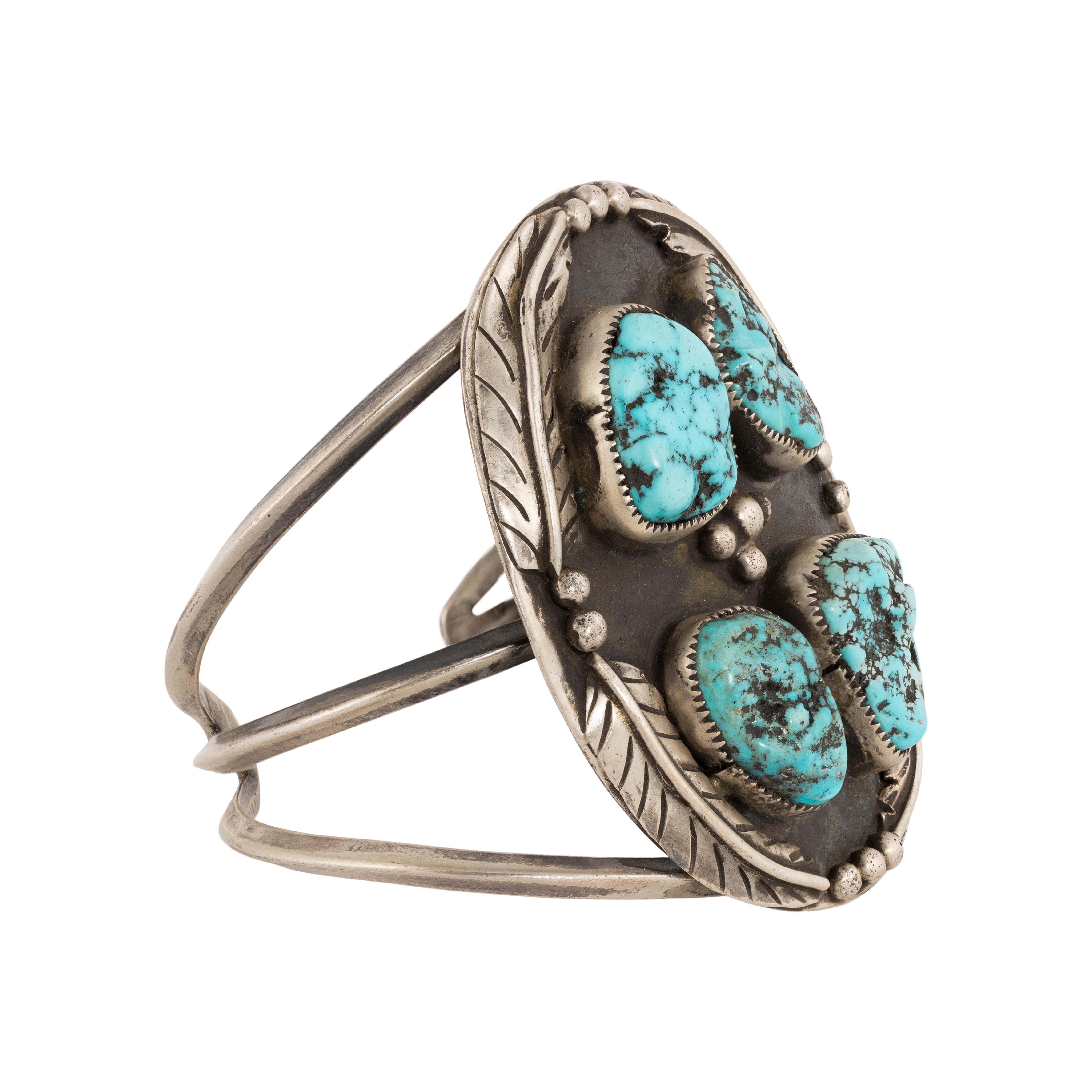Navajo Kingman turquoise bracelet. Four raised stones in shadow box designs surrounded by leaves and beads. Three thin bands molded into one. Heavy patina that can be buffed out easily to make shiny. Flexible enough to adjust to wrist. Great patina