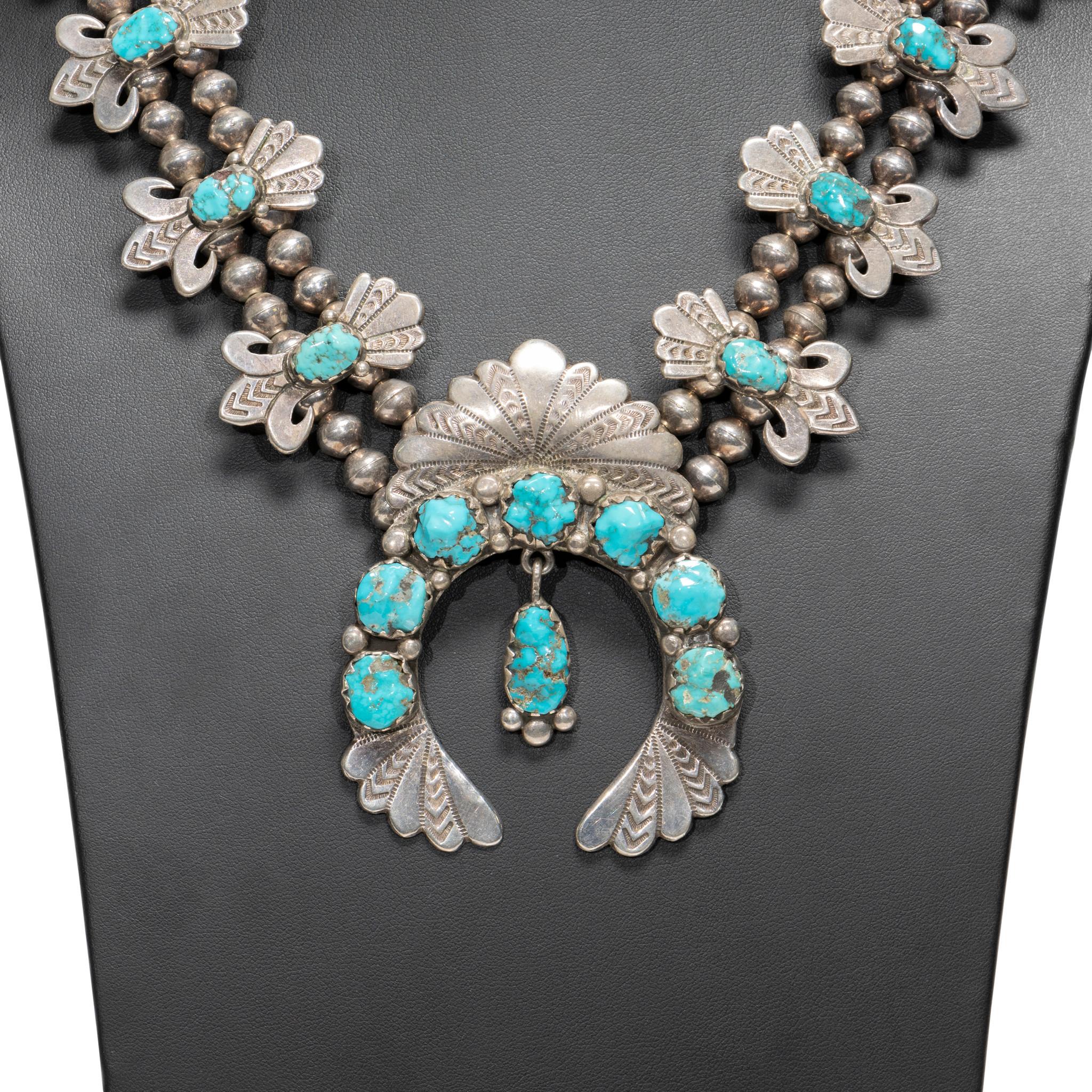 Navajo turquoise and sterling squash blossom necklace. 12 quality Kingman turquoise stones on each side with 7 stones on naja and another single naja drop. Each stone surrounded by hand stamped palmettes with mirrored design on naja. Maker's mark