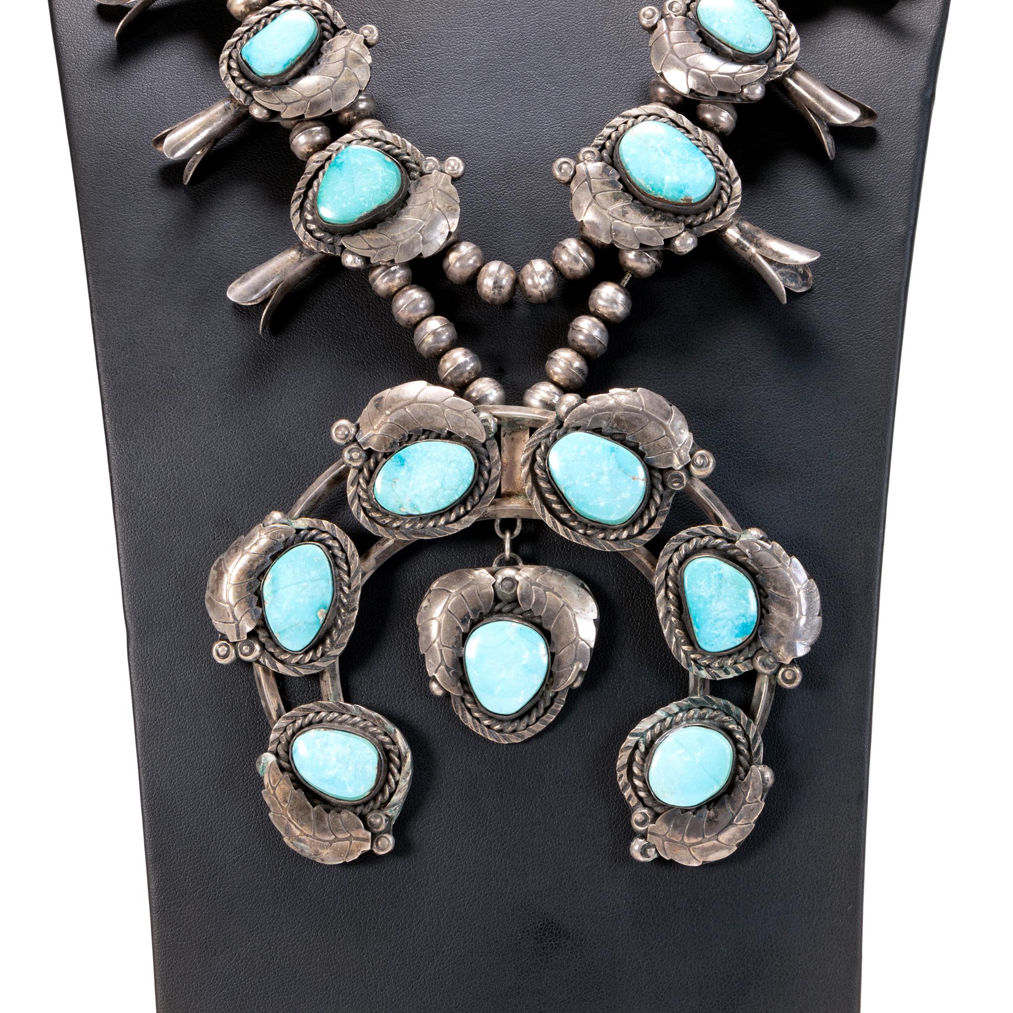 Large squash blossom necklace with 17 Kings Manassa turquoise nuggets and silver leaf setting. Each stone surrounded by twisted rope border, stamped beads, and sterling feather detail. Stones are a light blue with cloudy white matrix. Old Pawn.