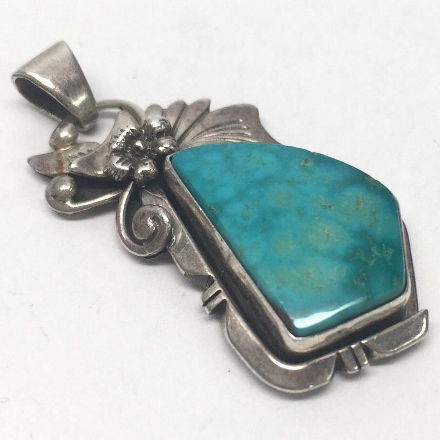 Navajo Les Baker sterling silver turquoise pendant by artisan Harry Sandoval. Above the stones is a small flower design.

Marking: BAKER L eagle B JEWELRY, H arrow S, STERLING. (faded in spots)

Measures approx. 1 1/2