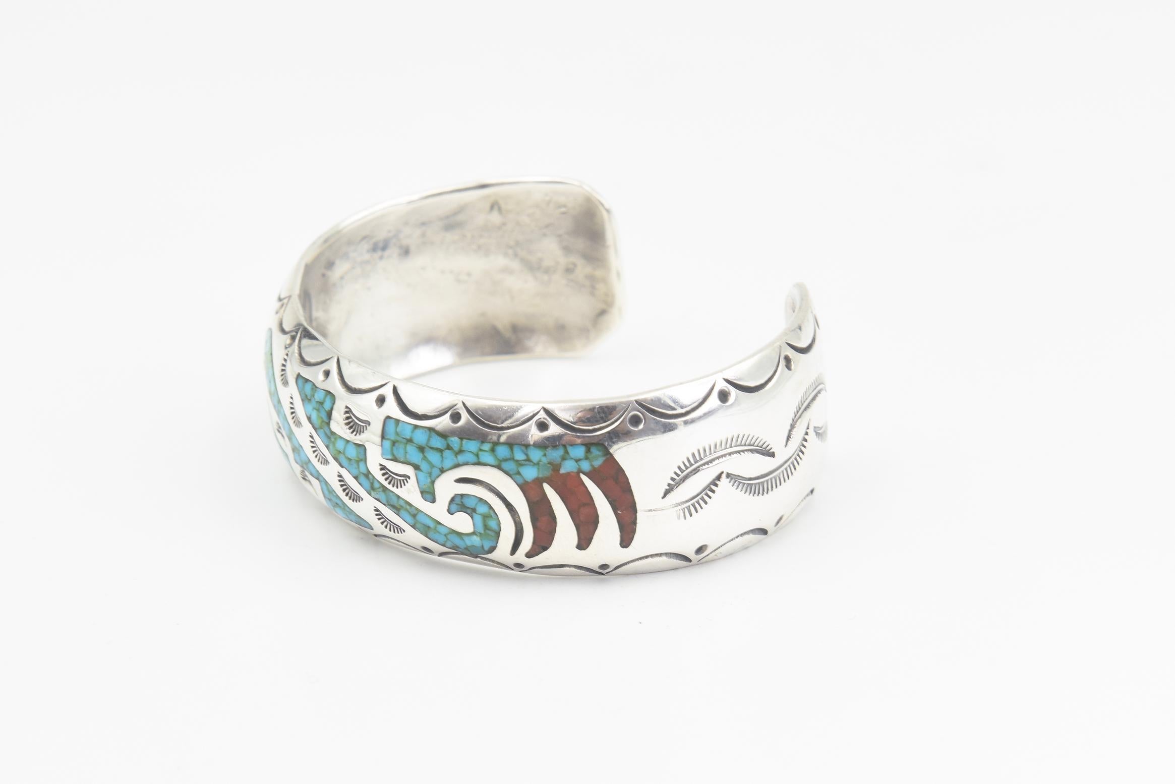 Native American turquoise and coral chip inlaid cuff bracelet created by Navajo artist Kenny Jack.  The design incorporates traditional  Navajo patterns and symbols.  The inlaid wings represent a thunderbird design.  Additional decoration includes