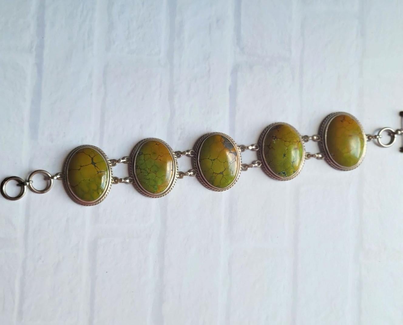 Ti presentiamo uno splendido bracciale d'argento vintage realizzato a mano dagli indiani americani Navajo e caratterizzato da uno squisito turchese Greene & Greene dell'Arizona. Il bracciale presenta cinque grandi cabochon di turchese verde naturale
