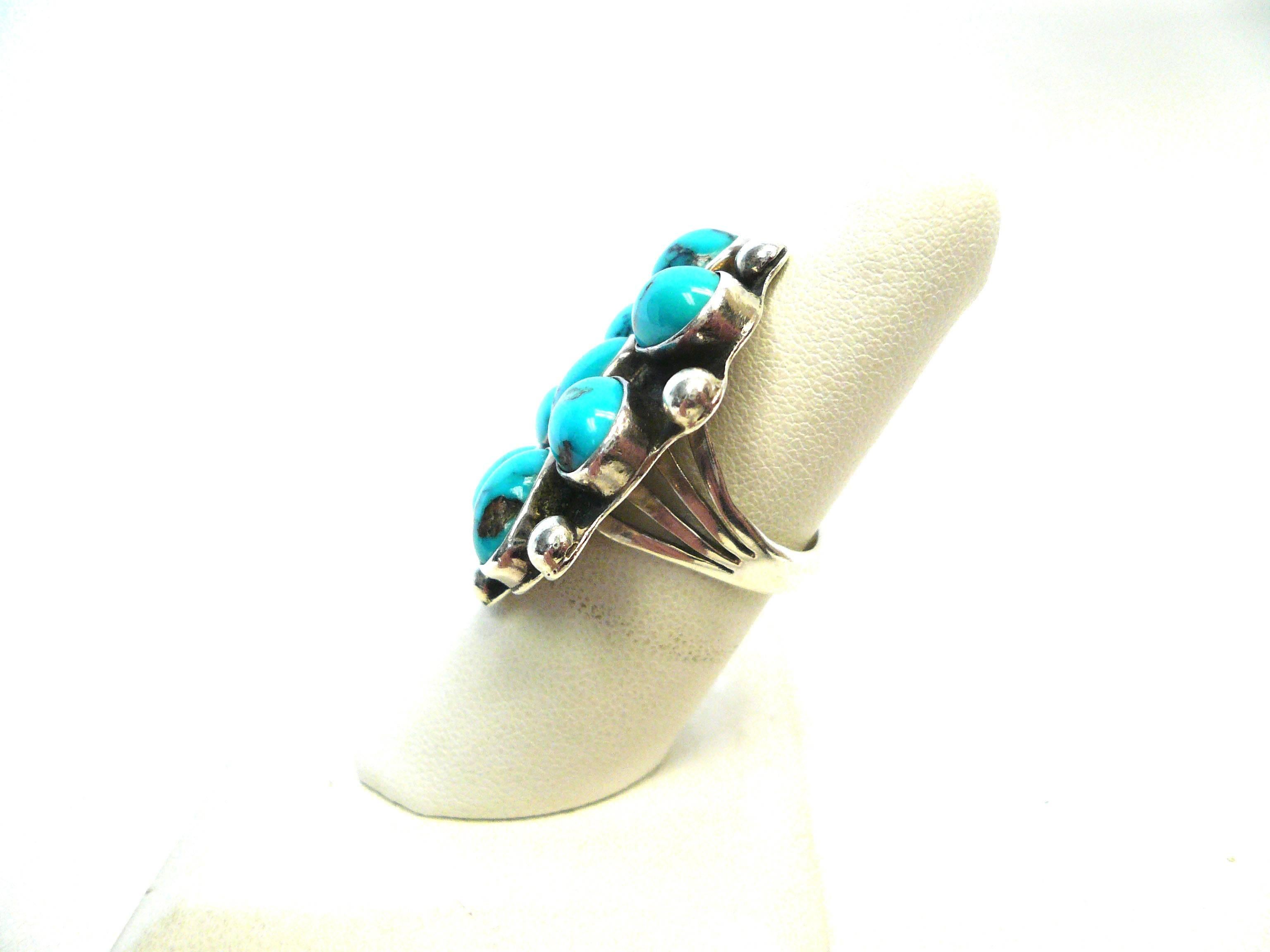 Lively ring is made of sterling silver and eight oval cabochon pieces of turquoise bezel set. Ring features rope details and a split shank design.
Ring is signed W. Yellowhorse. Yellowhorse is a third generation Navajo jewelry designer who's work is