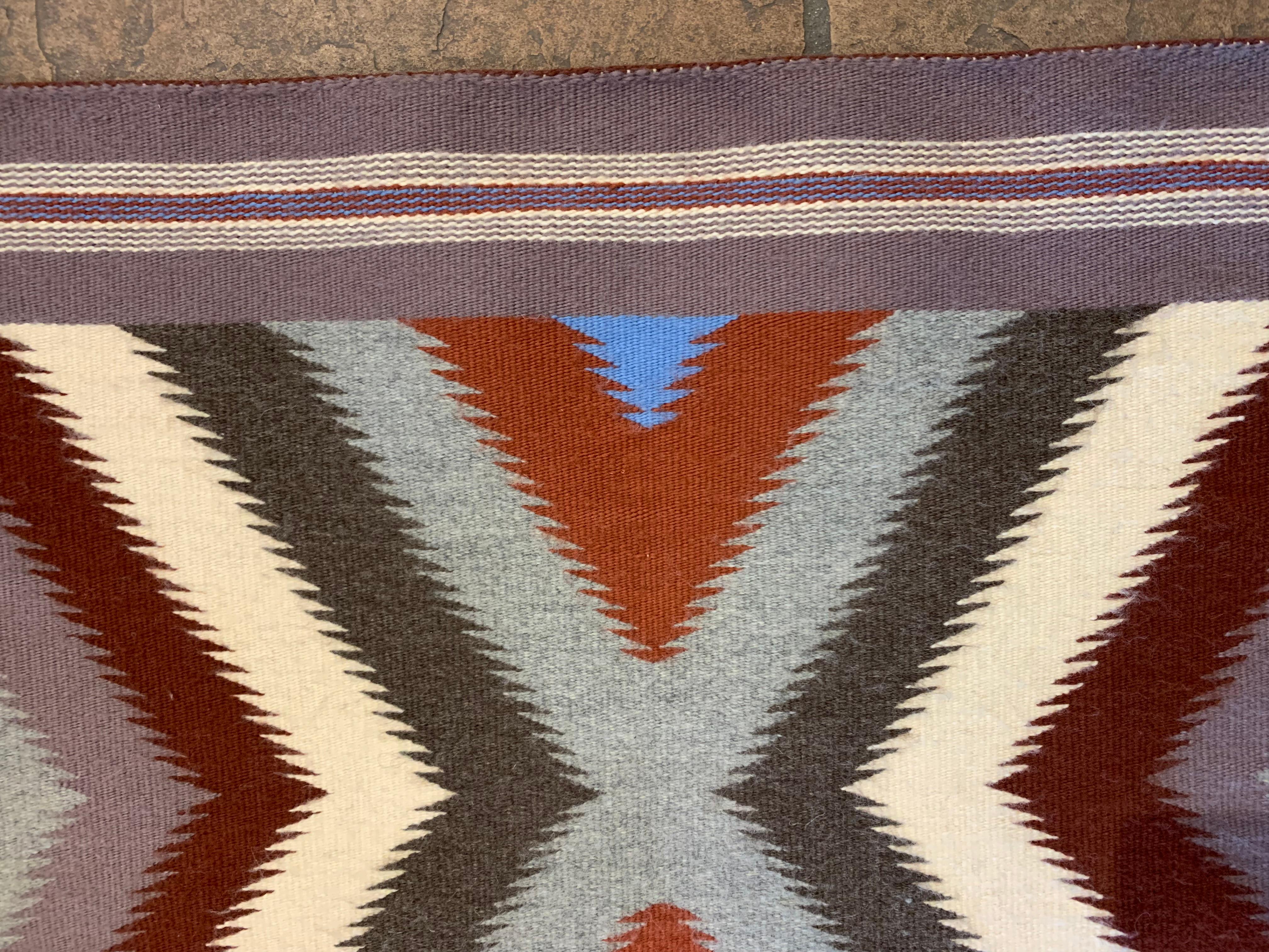 Red Mesa style Navajo rug with bands of gray, dark red, blue and white in triangular pastel patterns.  
This contemporary hand woven wool rug from the Four Corners area was woven in the 1990’s.  29” x 48”.   

Most of the Four Corners region belongs