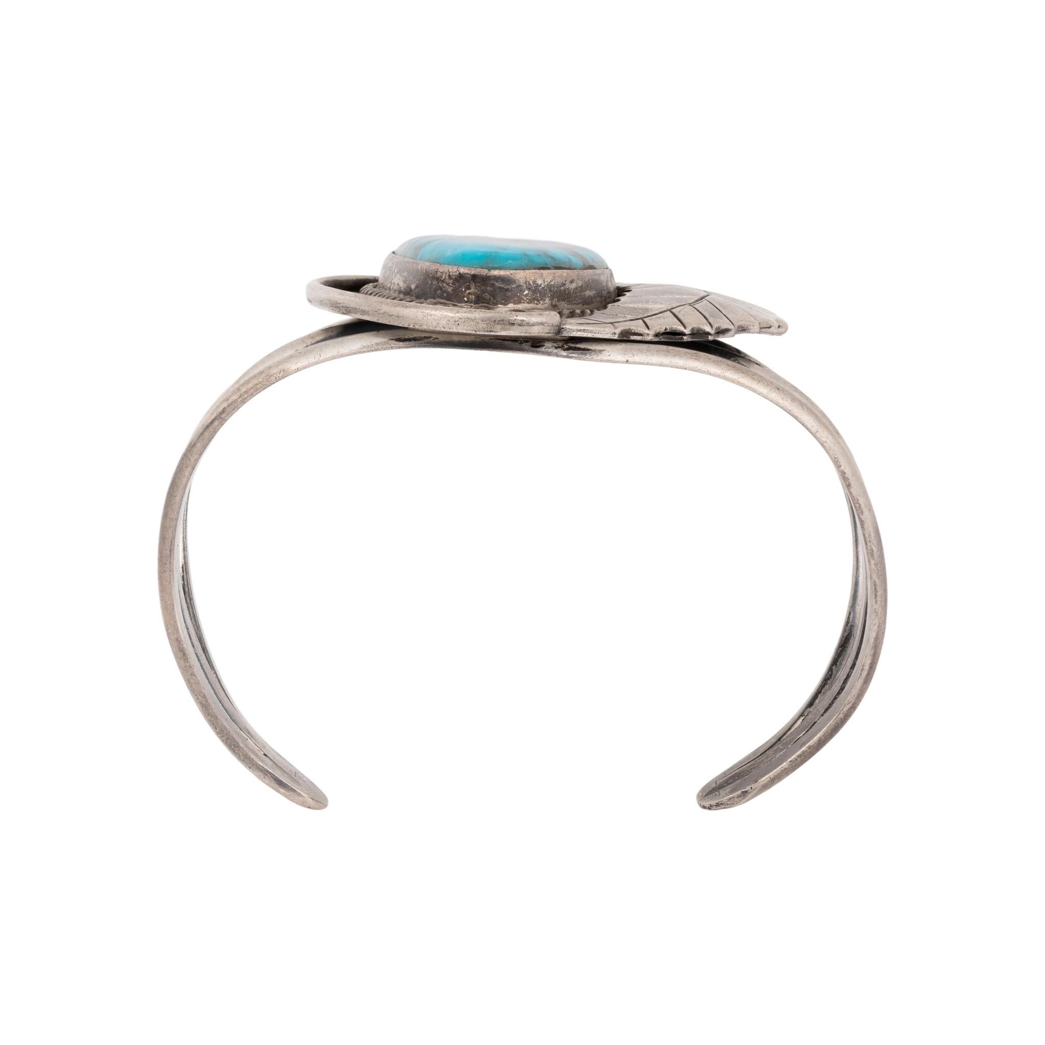Bracciale Navajo Kingman in turchese e argento sterling. Grande pietra centrale incastonata in un design a scatola d'ombra con bordo in corda ritorta e grande piuma laterale. La pietra è di un bel blu brillante con matrice scura e quarzo. La pietra