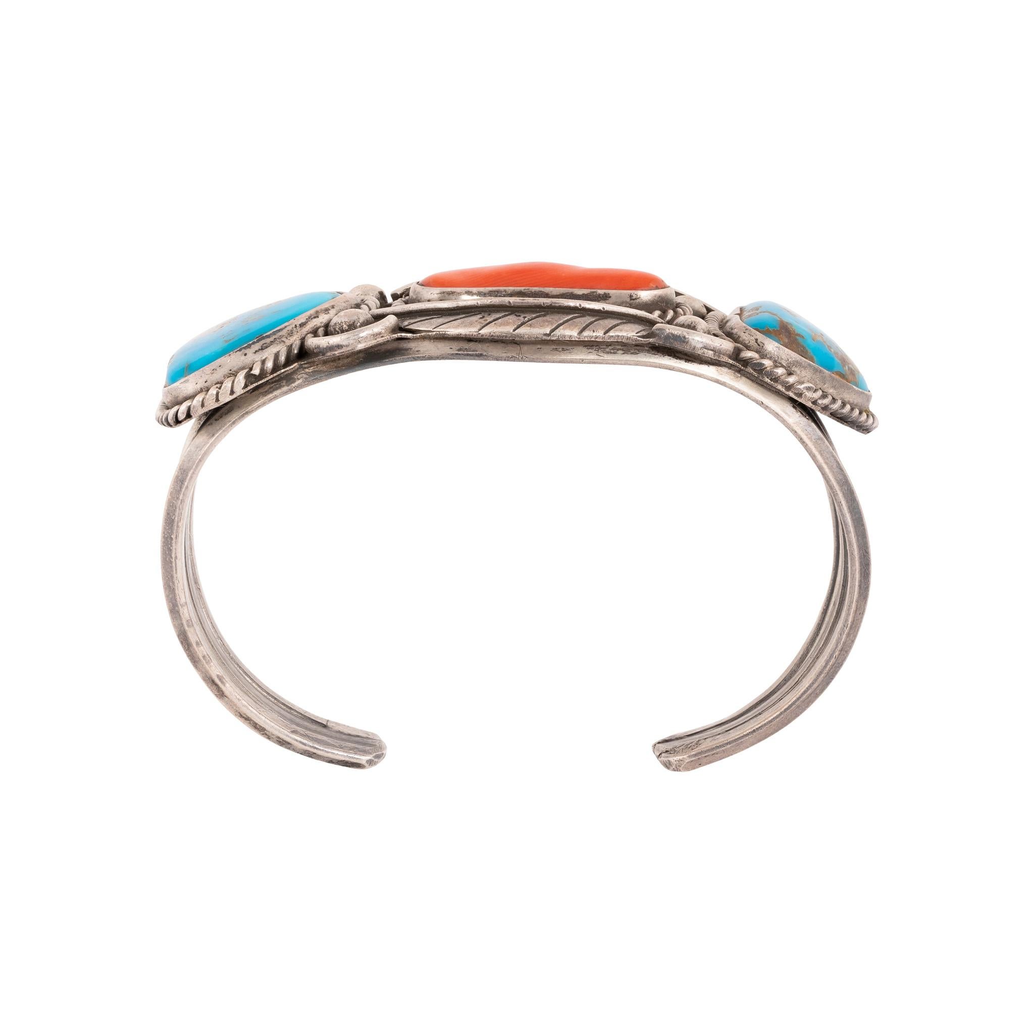 Bracciale Navajo Sleeping Beauty in turchese e corallo. Incastonato in argento sterling con due pietre triangolari di turchese e un ramo centrale di corallo. Bordi in corda intrecciata, perline Navajo e disegno di foglie. Ottima patina e una certa