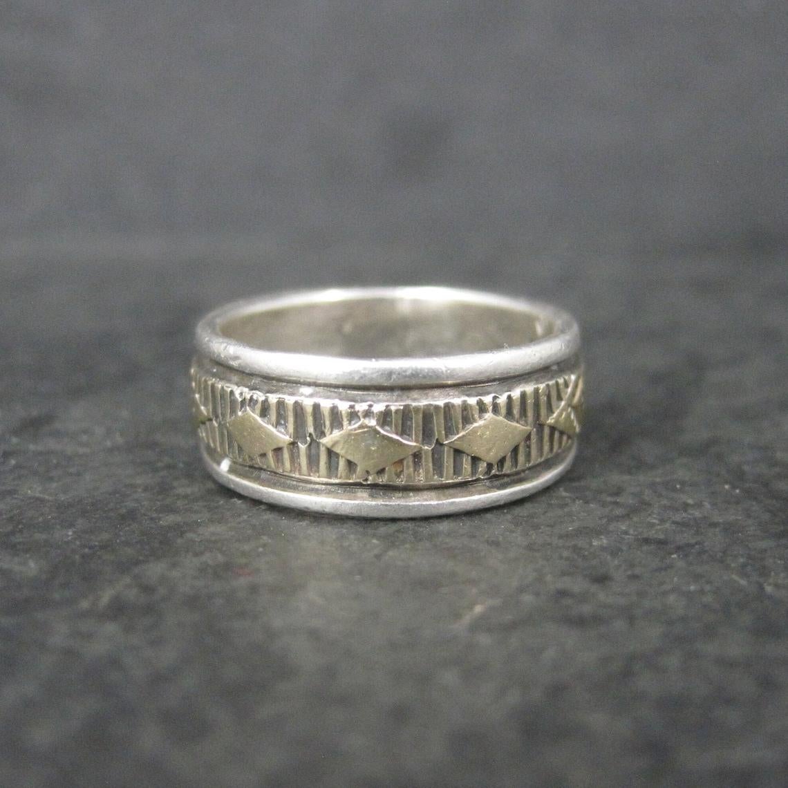 Dieser wunderschöne Ring im Vintage-Stil ist eine Kombination aus Sterlingsilber und 14 Karat Gelbgold.
Es ist eine Kreation des Navajo-Silberschmieds Bruce Morgan.

Abmessungen: 7,5 mm breit
Größe: 6,75, passt aber aufgrund der Breite eher wie eine