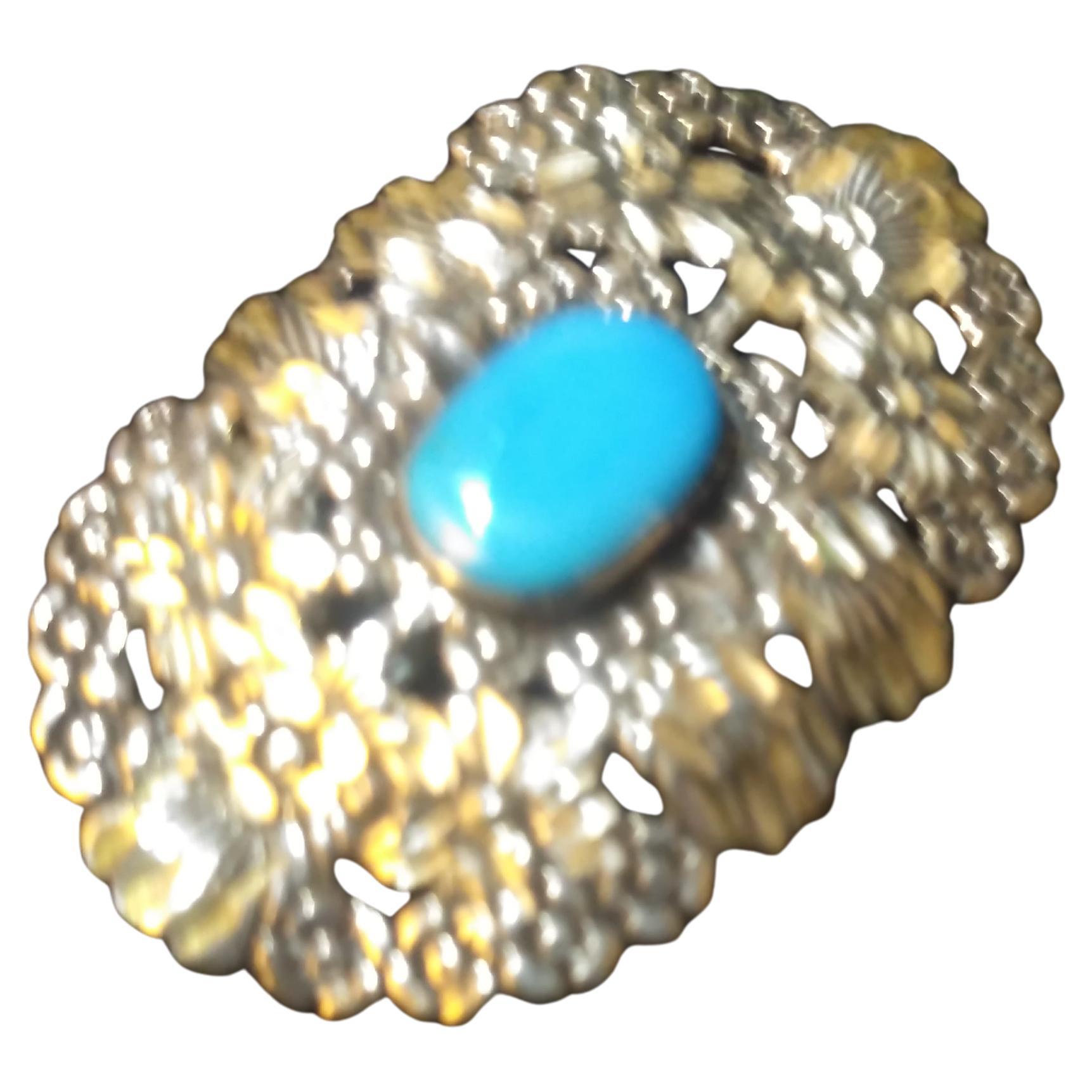 This is a very detailed piece of jewelry. It's  of Native American origin. It's made of sterling silver and has an oval turquoise stone setting. The silver craftsmanship is quite exquisite.