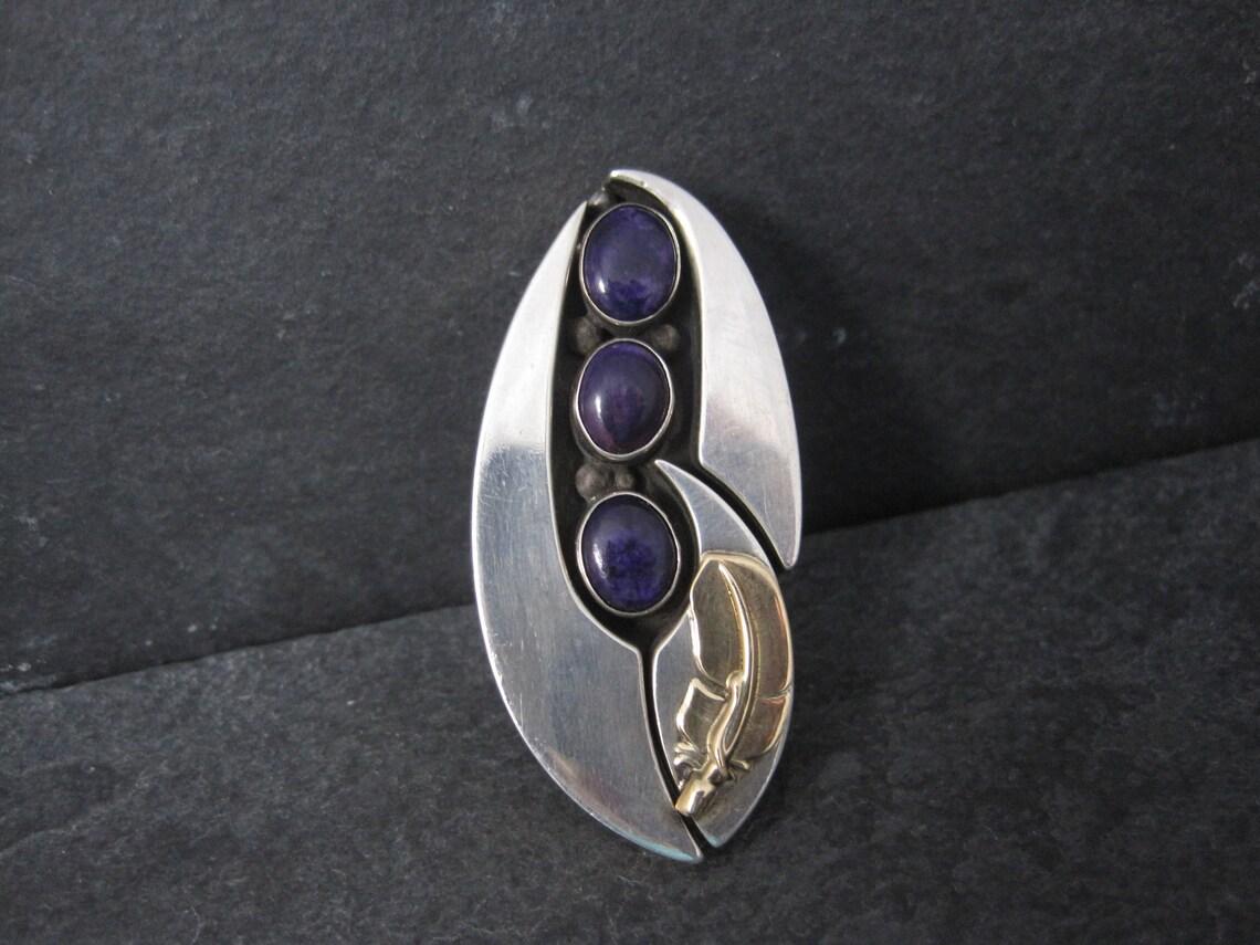 This stunning, massive ring is a one of a kind custom creation by the talented Wilbert and Cora Vandever.

Its sterling silver with a 14k yellow gold feather and 3 beautiful 8x10 sugilite gemstones.

The face of this ring measures 1 1/16 inches east