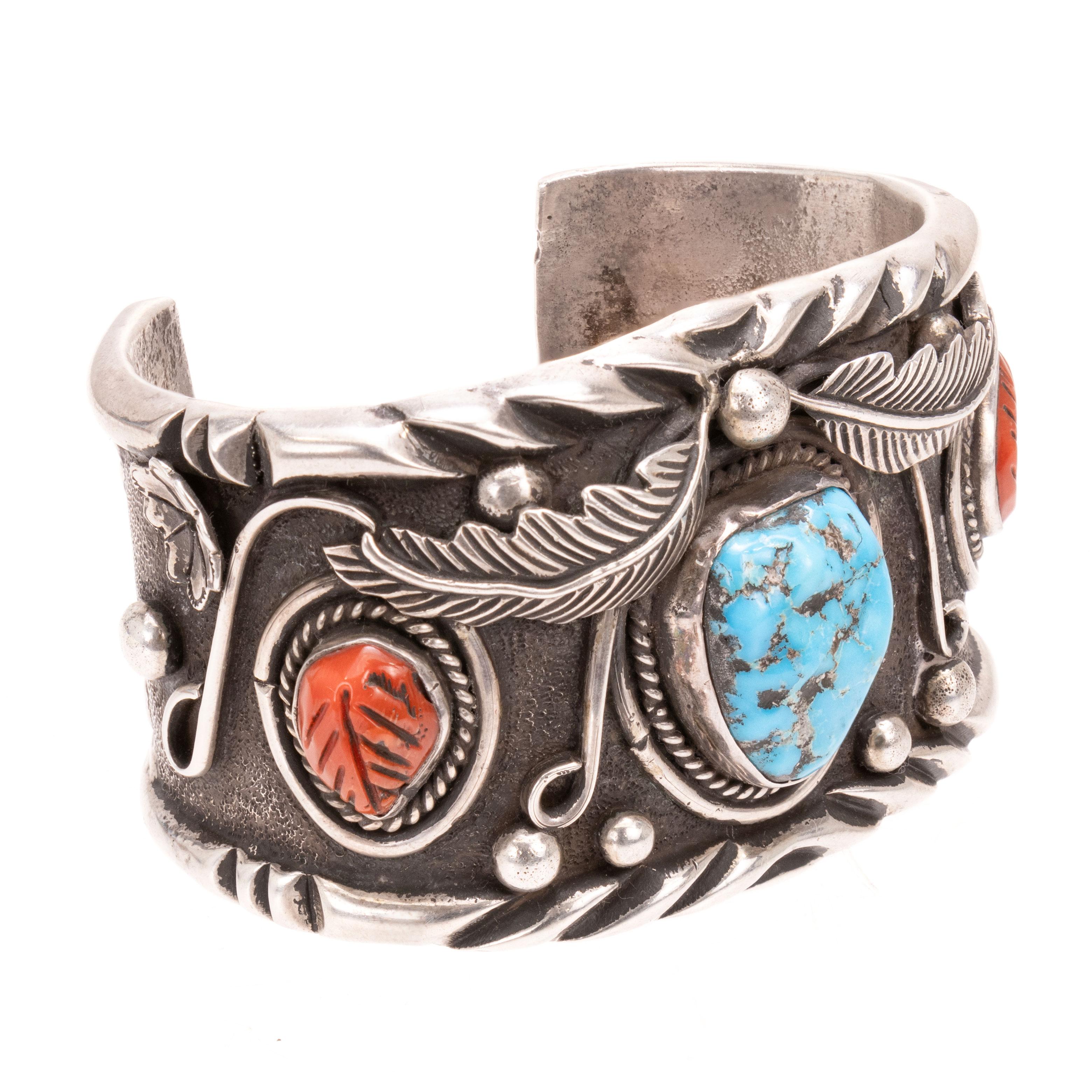 Bule diamond turquoise and coral bracelet on sturdy sterling silver cuff. Each stone framed by twisted rope border and leaf design etched into each coral stone. Stones are surrounded by leaf, scrolled, and sterling bead designs. Stamped on back