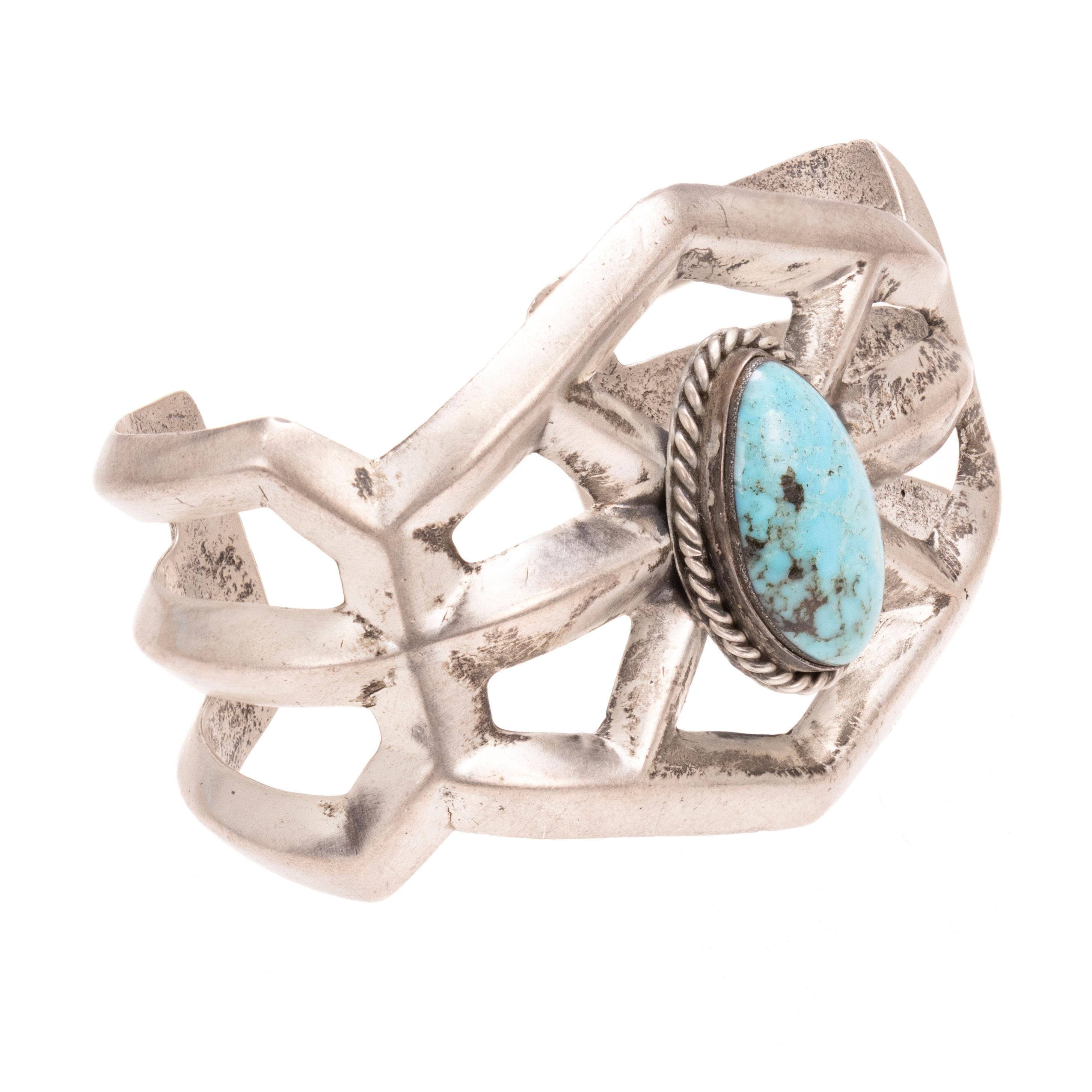 Bracciale in turchese Navajo e argento sterling. Single Stone con incastonatura a castone, circondata da un bordo in corda ritorta. Il turchese è un blu chiaro con matrice bianca e scura. Incastonato in un elaborato bracciale in sabbia/ Non marcato.