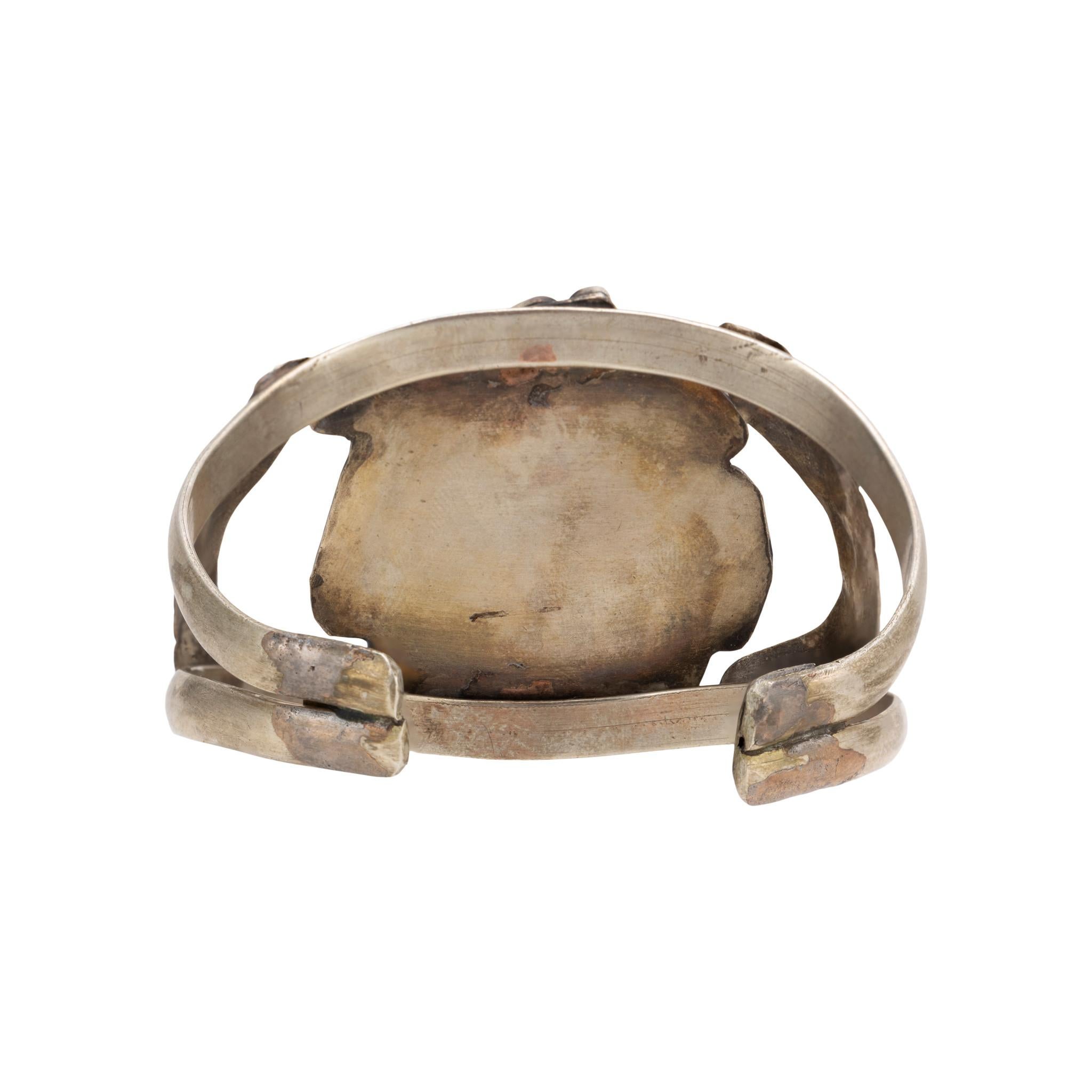 Pulsera brazalete de turquesa Navajo Kingman y plata de ley. Single Stone engastada en un diseño de caja de sombra con borde de volutas. enmarcada por una sola pluma a cada lado. Engarzado en puño de doble banda. Suficientemente flexible para