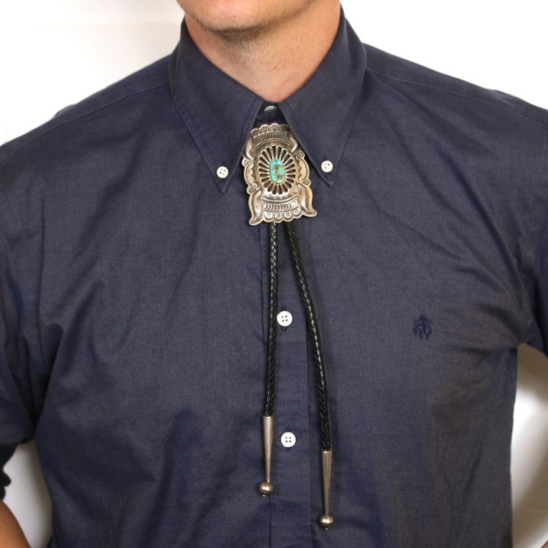 Celebrate your Native American heritage with this eye-catching bolo tie. Created in sterling silver by Navajo craftsman Ernest Bilagody, this piece features a genuine turquoise and traditional Southwestern artistry. The bolo itself is dark braided