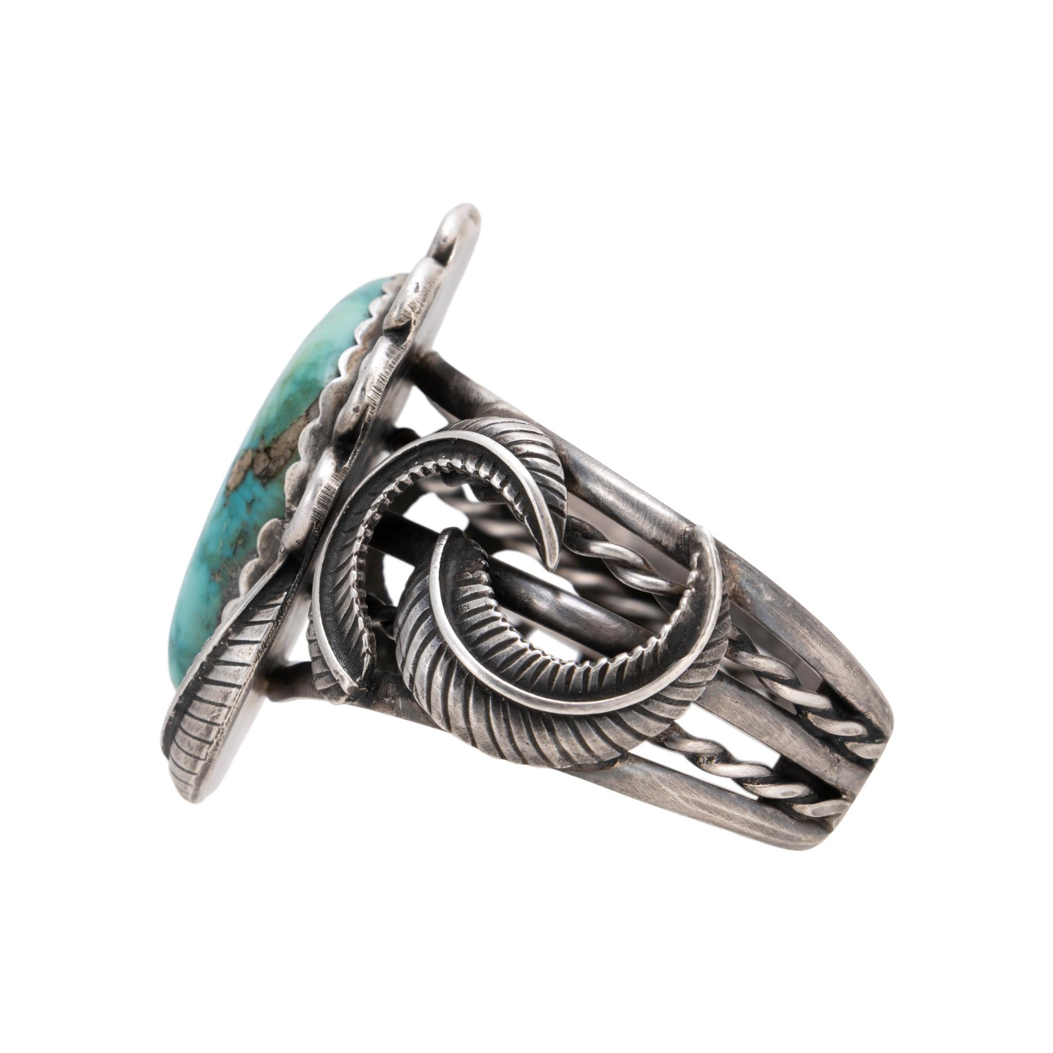 Pulsera brazalete de turquesa de las Montañas Indias Navajo y plata de ley. Piedra grande, natural y sin tratar, rodeada de un borde de cuerda retorcida y hojas en relieve. La piedra es de un hermoso azul intenso con matriz y cuarzos de un azul más