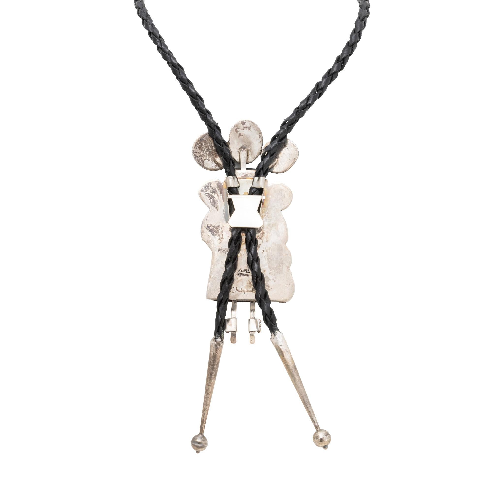 Cravatta bolo a tema Kachina con abbellimento aggiunto. Il design Kachina è evidenziato da sei cabochon di turchese naturale non trattato di Nature che riposano in castoni d'argento a dente di sega. Al centro, una figura d'oro con accenti di pietre