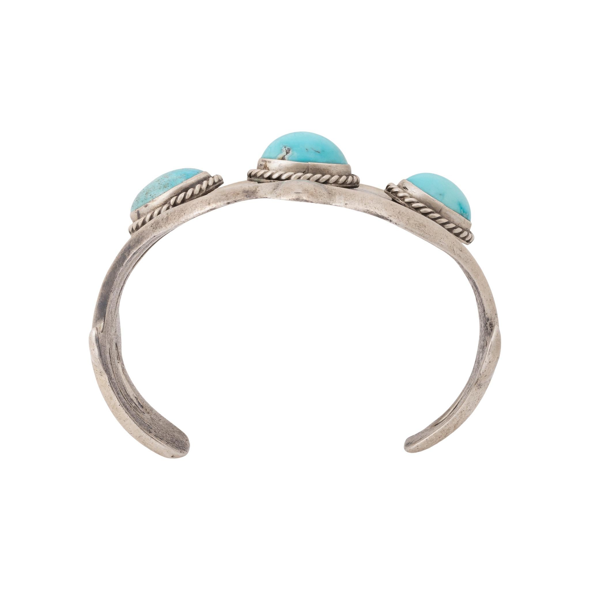 Pulsera Navajo de plata fundida y turquesa de la Bella Durmiente. Tres bellos ejemplares de turquesa Bella Durmiente, azul claro con matriz mínima o nula. En engaste biselado con borde de cuerda retorcida, engastado en puño de fundición de arena de