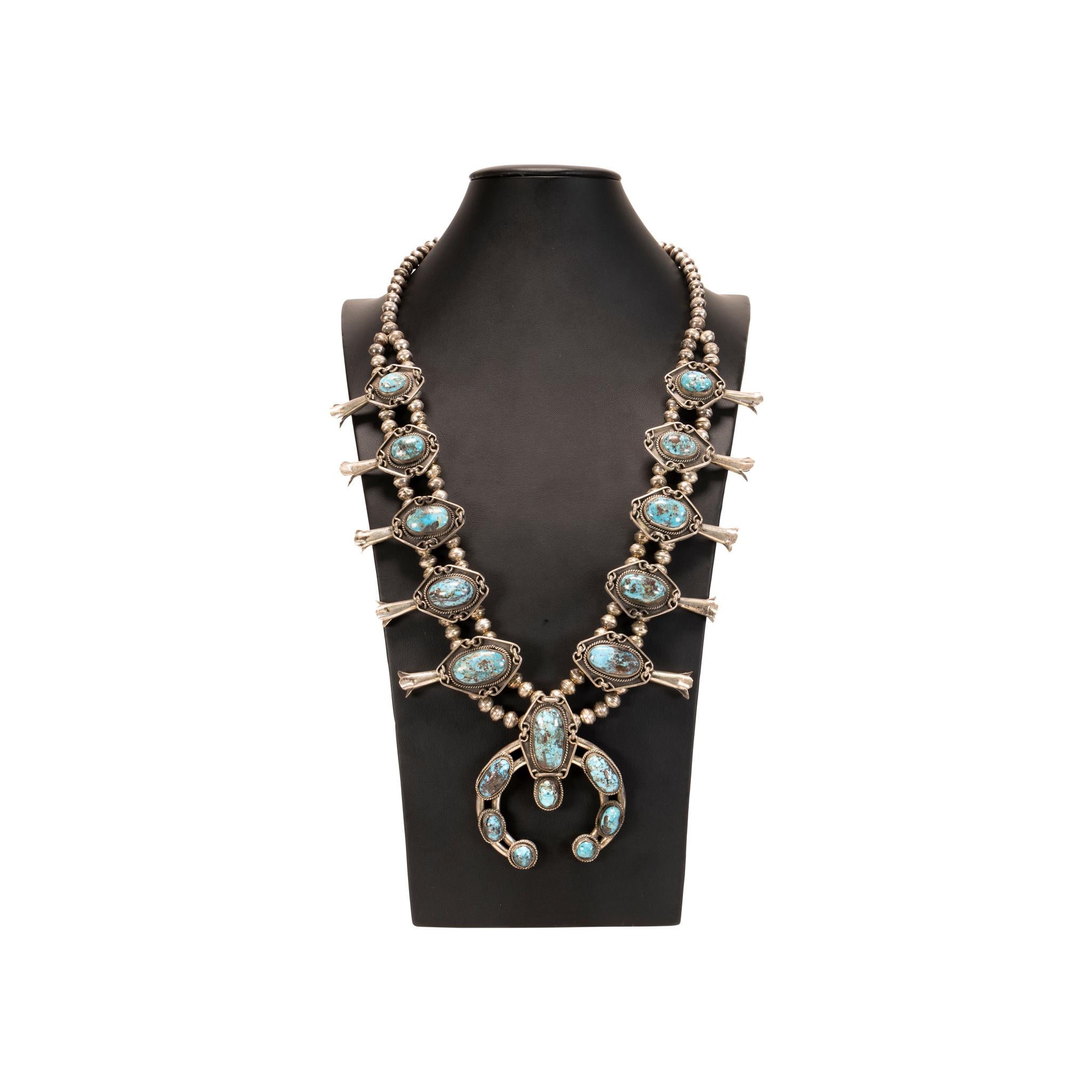 Navajo sterling silver and Easter Blue turquoise squash blossom. Ten quality, natural stones set in twisted rope and shadow box designs ending in an additional eight stone naja. No maker's mark. Great patina. 

The Navajo word for the squash blossom