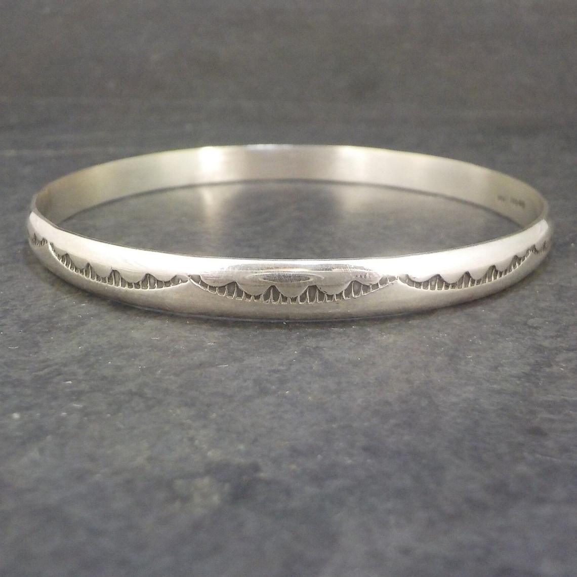 This beautiful Southwestern bangle bracelet is sterling silver.
It is a creation of the Navajo, Tahe family.

Measurements: 6mm wide - Inner circumference of 7 1/2 inches - Inner diameter of 2 1/2 inches
Weight: 17.7 grams

Marks: Sterling,