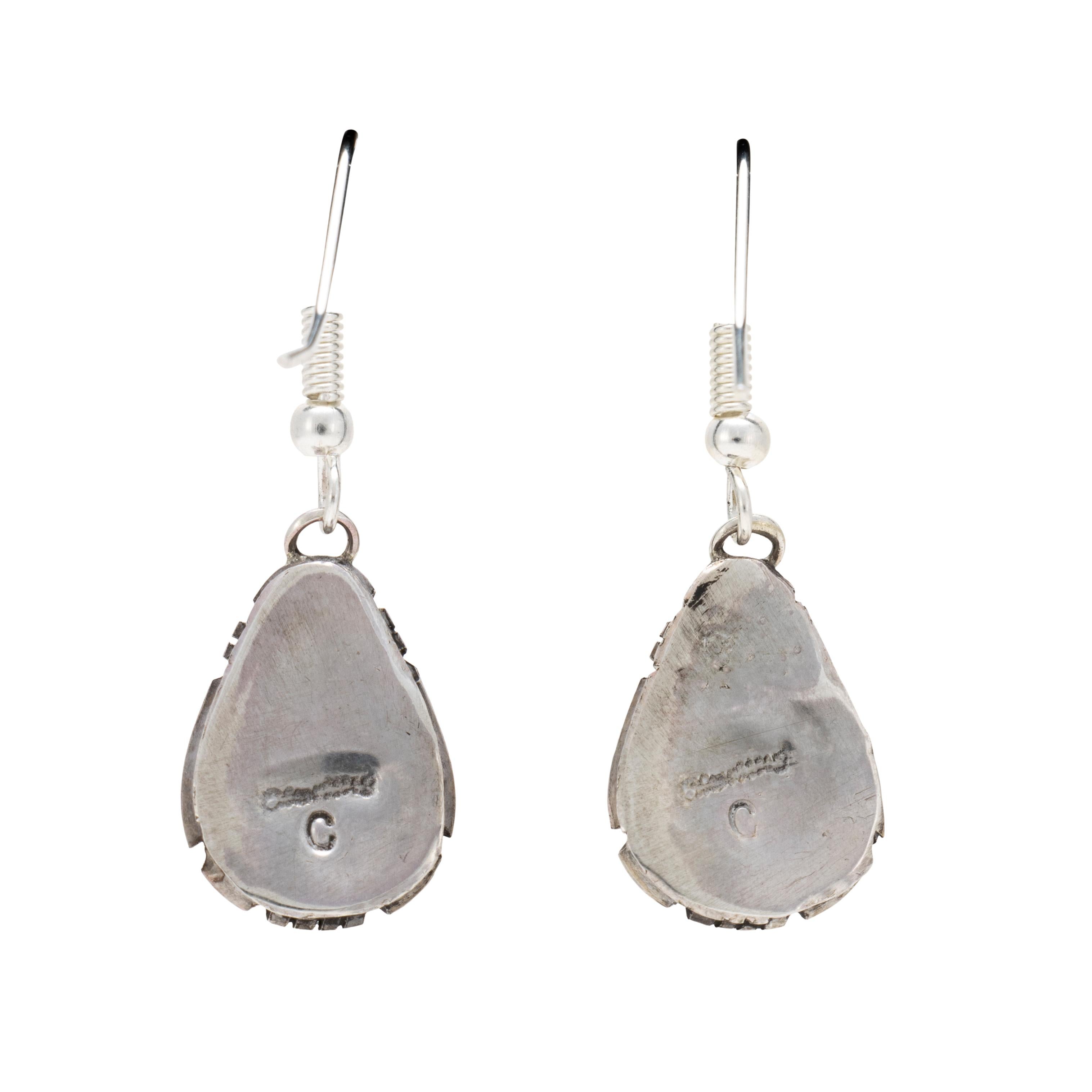 Orecchini pendenti in turchese di bufalo bianco del Navajo. Pietra tagliata a goccia in castone liscio con bordo tratteggiato, sospesa a ganci a forma di amo. Le pietre sono di un colore bianco e nero intenso con un'ottima matrice. Realizzato