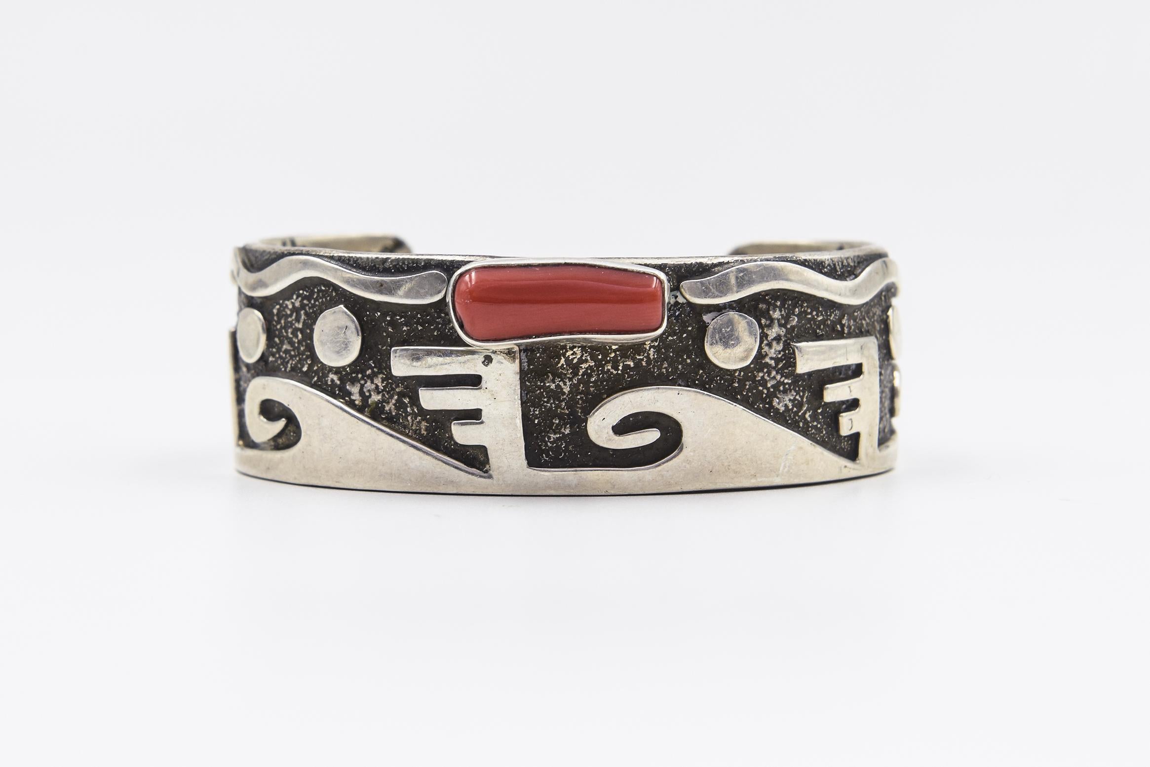 Der Navajo-Zuni-Indianer Alex Sanchez ist für seine Petroglyphen-Designs aus Sterlingsilber bekannt. Dieses atemberaubende Manschettenarmband ist ein perfektes Beispiel für seine Arbeit, die auch einen roten italienischen Korallenakzent aufweist. 