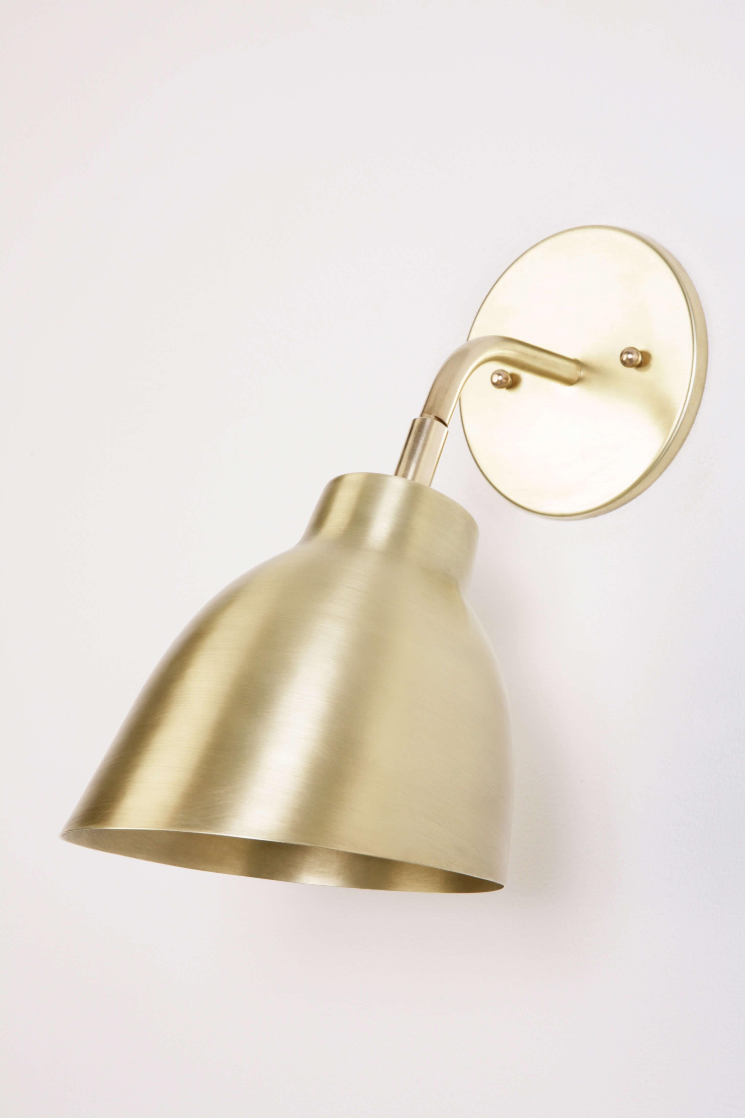 The Navire petite sconce is part of Atelier de Troupe's Classic Navire collection inspired by nautical lamps from the 1930s. It has a solid brass arm and up and down tilting shade. The sconce is hardwired and equipped with a 60W medium base