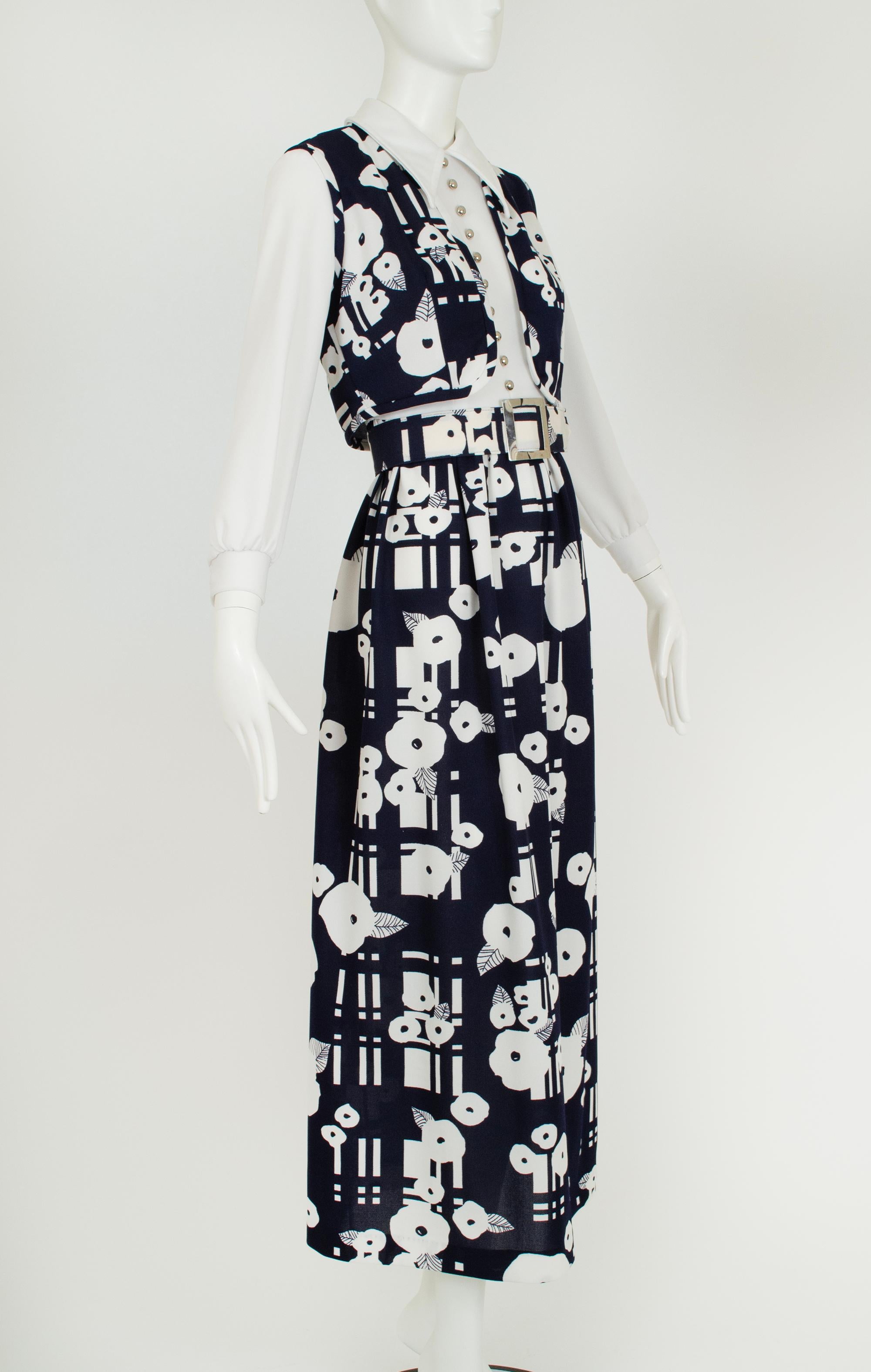 A groovy maxi dress whose dizzying print is balanced by its conservative cut. Sweetly subversive and thoroughly retro.

Long sleeve maxi hostess dress with white wing collar bodice and navy and white graphic print maxi skirt; decorative domed silver