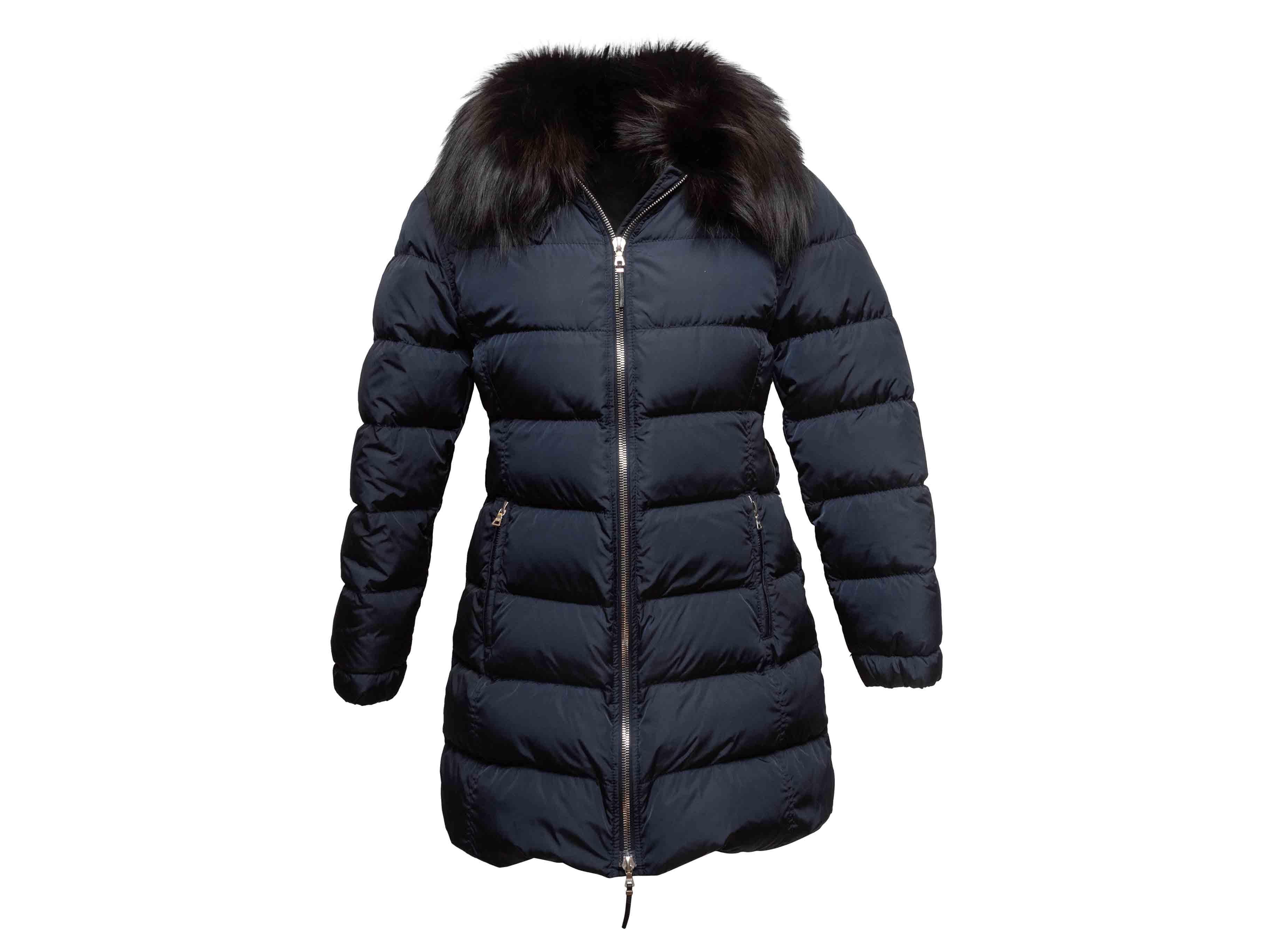Navy down hooded puffer coat by Prada. Black fox fur trim at hood. Dual hip pockets. Zip closure at front. 38