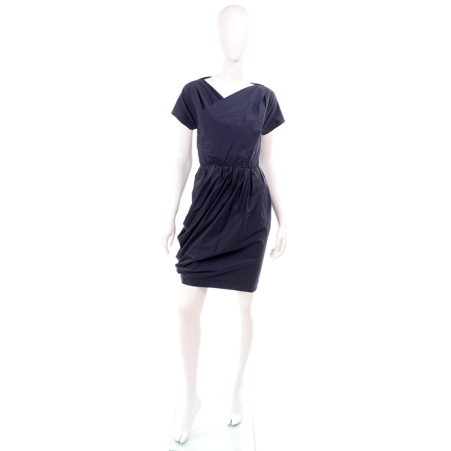 This is a really wonderful Carven dress with a unique wrap style, ruching and an open back. This navy blue cotton dress closes with a side zipper and the draped  fabric layer secures on the right side with hooks and eyes. The dress has short sleeves