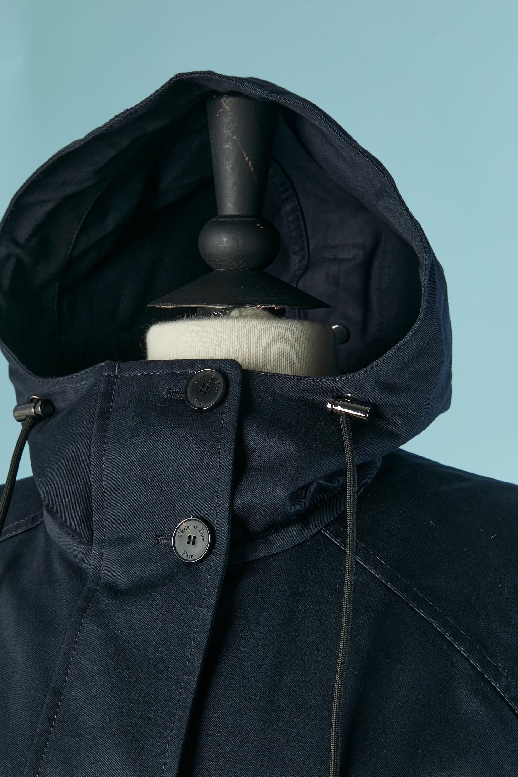 Parka in cotone blu navy con cappuccio e tasca. Chiusura con zip nascosta sulla parte centrale del davanti + bottone e asola sulla parte superiore. 4 tasche sul davanti con chiusura a bottone e asola con marchio. Una tasca sul lato sinistro. Una