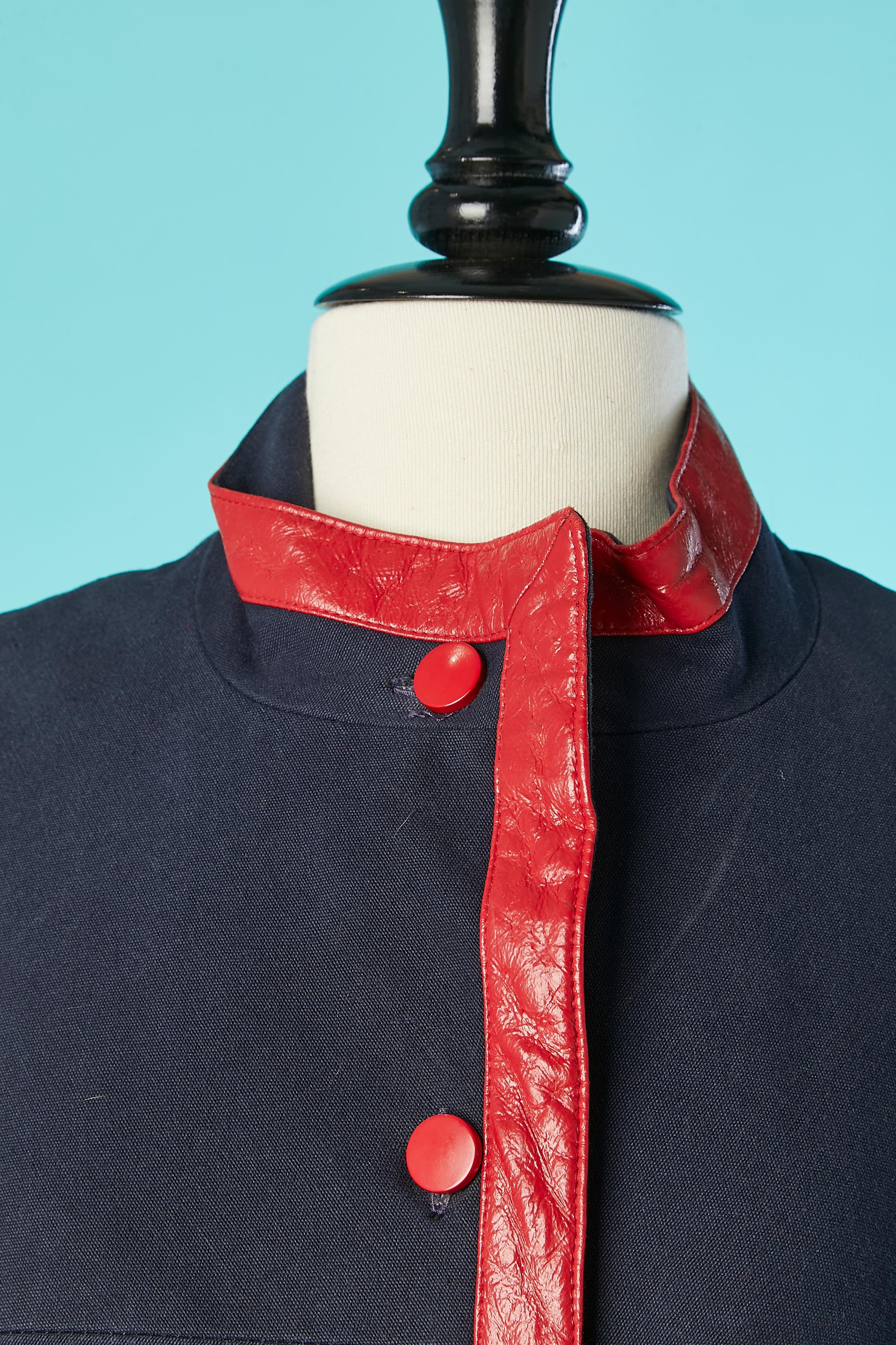 Manteau en coton bleu marine à simple boutonnage avec passepoil en PVC rouge. Pas d'étiquette de tissu mais la doublure est probablement en acétate. 
TAILLE M 