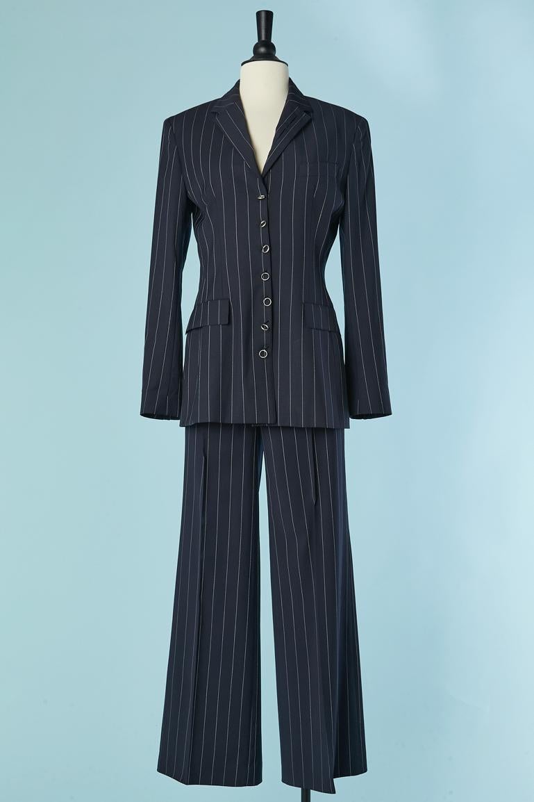 Navy blue pin-striped trouser-suit with metallic piercing  ( metalic rings) closure on the middle front and on the cuffs.
Main fabric: 100% wool. Lining: 60% acetate, 40% rayon. 
Shoulder pad. POCKET ON BOTH SIDE; 
size 42 (It) 38 (Fr) for the