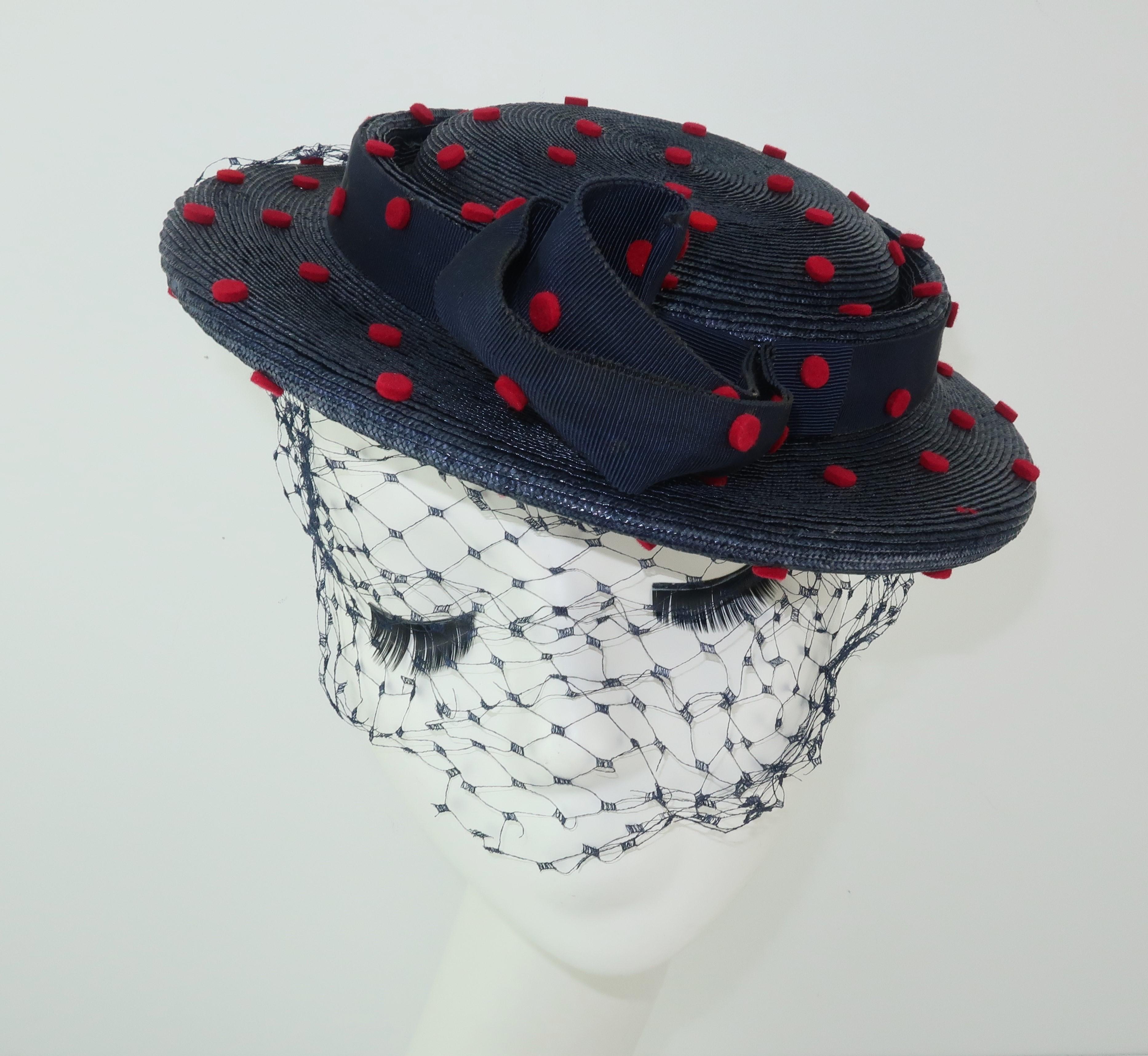 Sweet little C.1950 navy blue straw tilt style hat with red felt polka dots and a coordinating net.  The brim is whimsically decorated with grosgrain ribbon wired to create curlicues.  Original price tag attached from del Rogia of Atlanta, Georgia