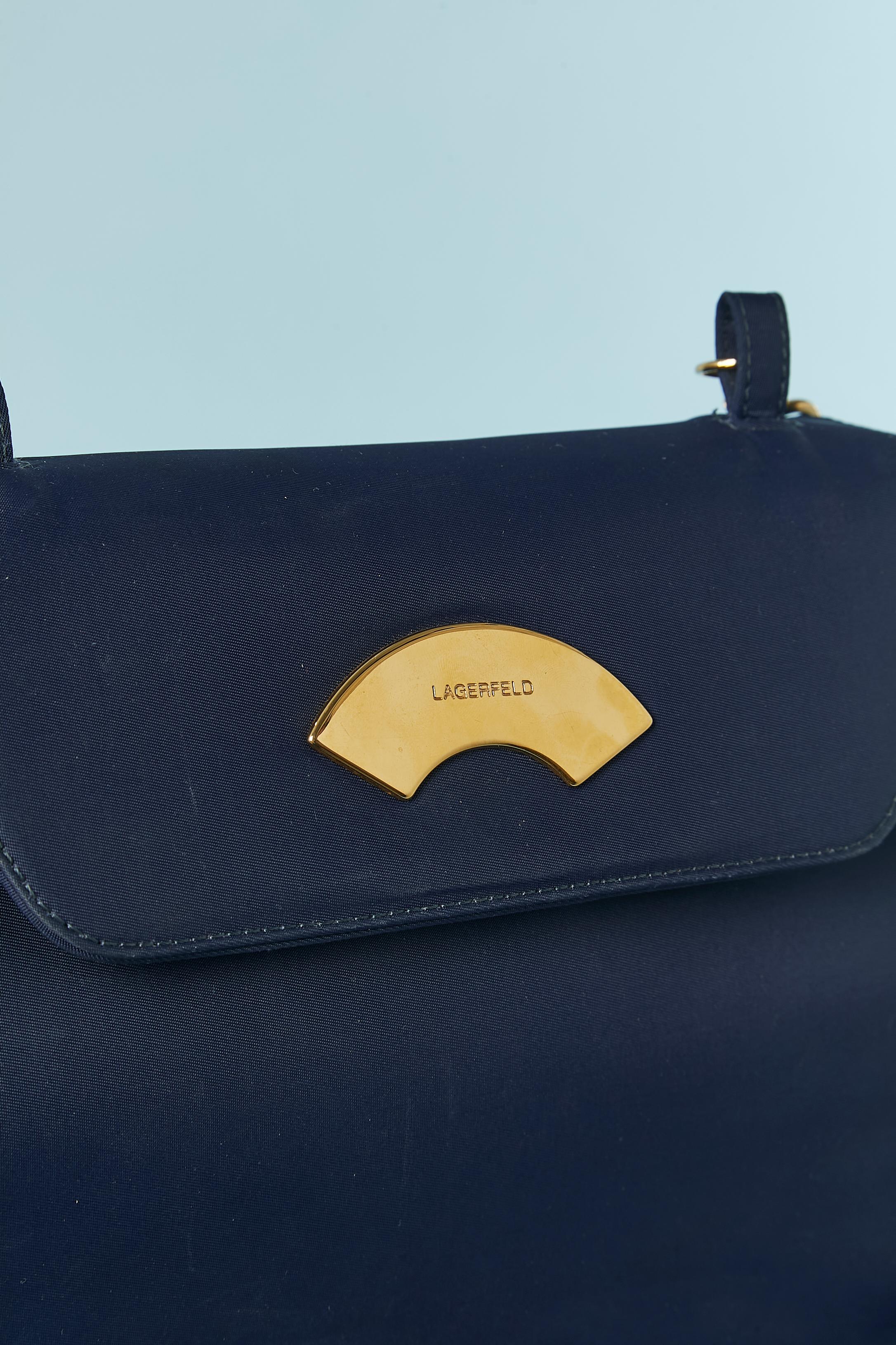 Navy blue structured shoulder bag. Snap closure in the middle front under the top flap. Detachable shoulder strap. 1 inside pocket with zip closure. No fabric tag composition but the main fabric is probably nylon. And the branded lining is probably