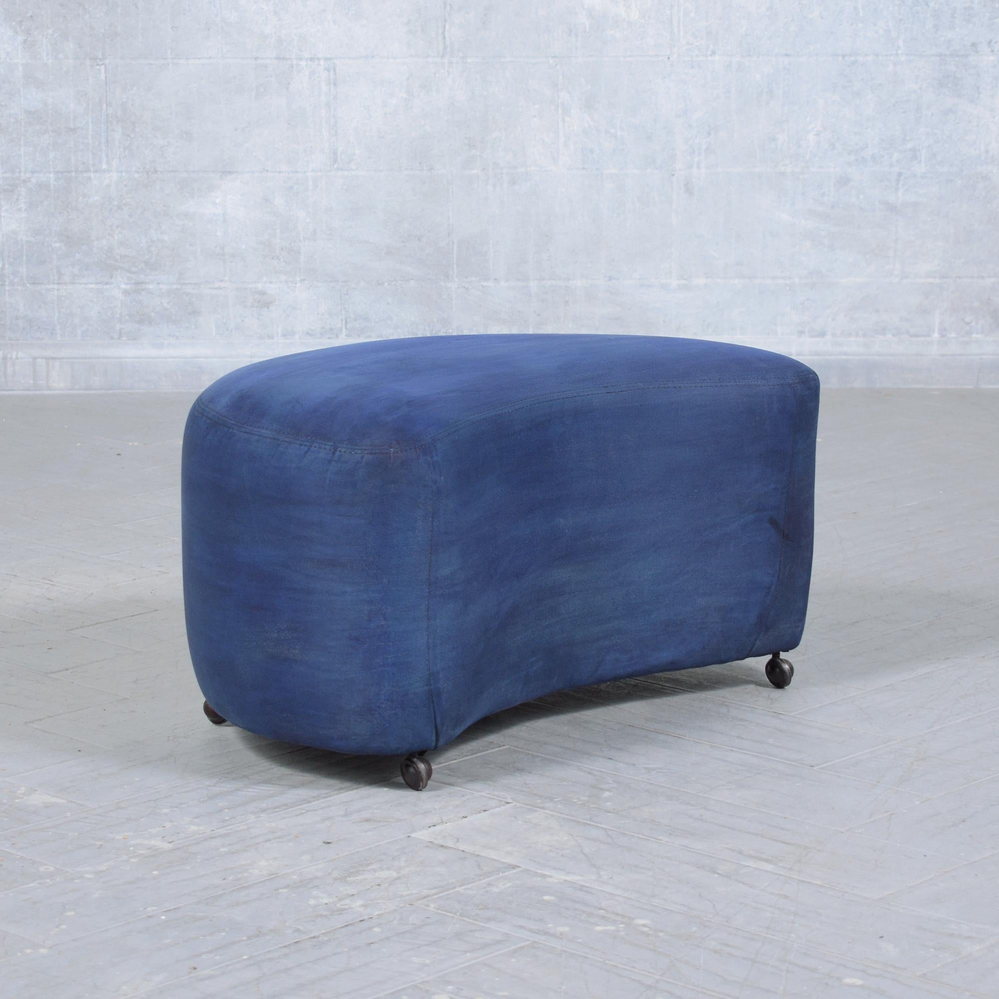 Introducing our Mid-Century Modern ottoman, hand-crafted from wood and in great condition. This unique ottoman showcases a standout design, adorned with a navy blue suede fabric and fine topstitched finishing details. Resting on round, black-colored