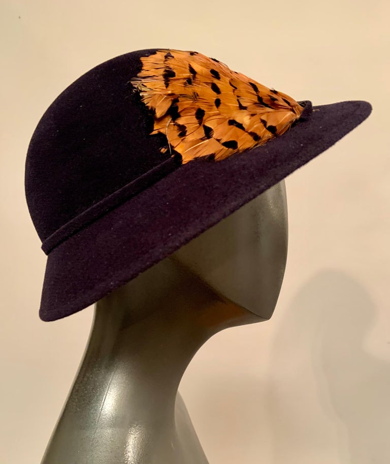 A chic navy blue wool felt hat is trimmed with a feather cluster on the right side,  The hat band and brim edge are made from the same fabric as the hat. It is in excellent condition.
Measurements;    Interior circumference 21.5