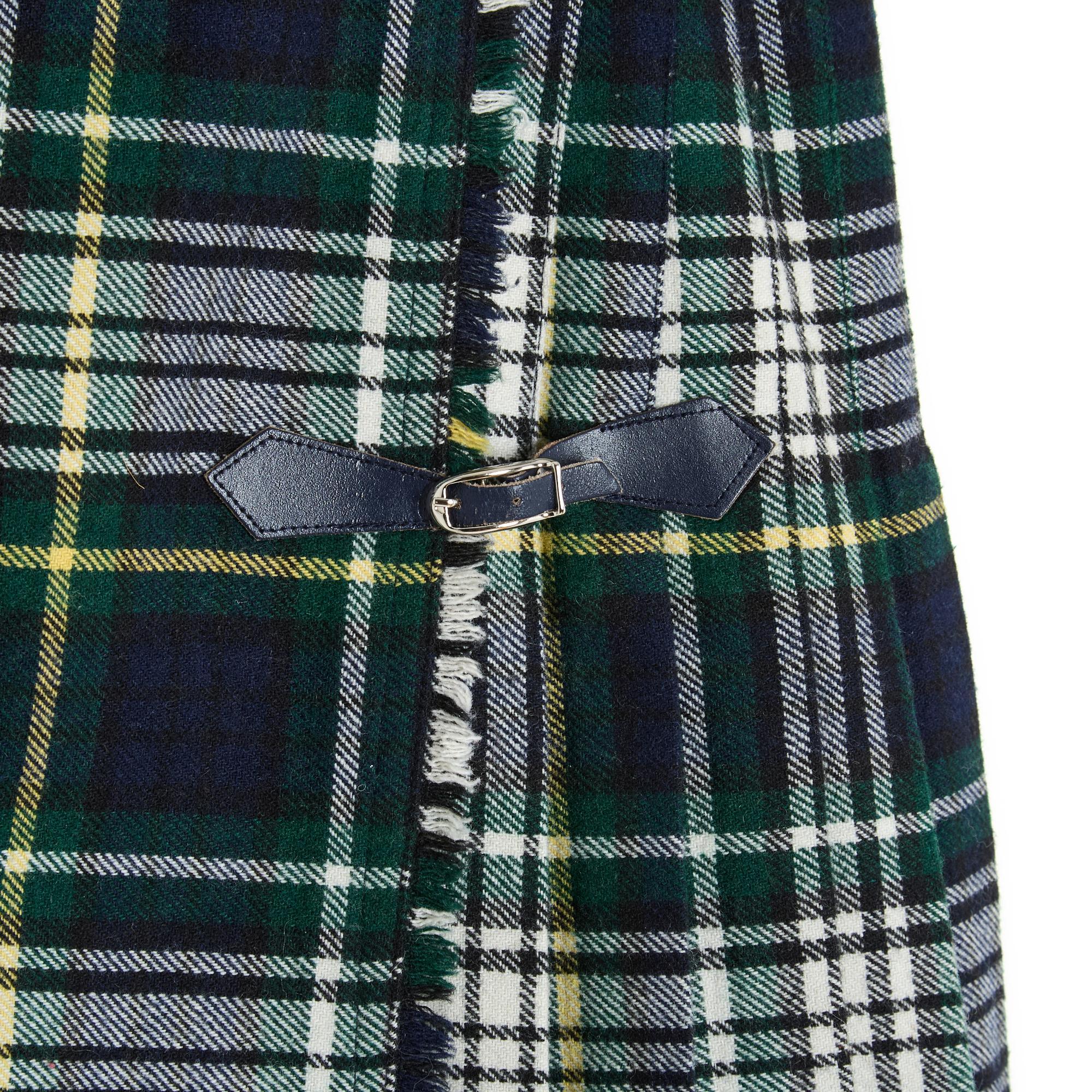 Short, pleated kilt-style wrap skirt in wool blend with tartan or check pattern, in shades of navy blue, green and ecru. Waist closed with a button on one side and two navy blue leather tabs on a silver metal pin buckle, unlined. No more size label