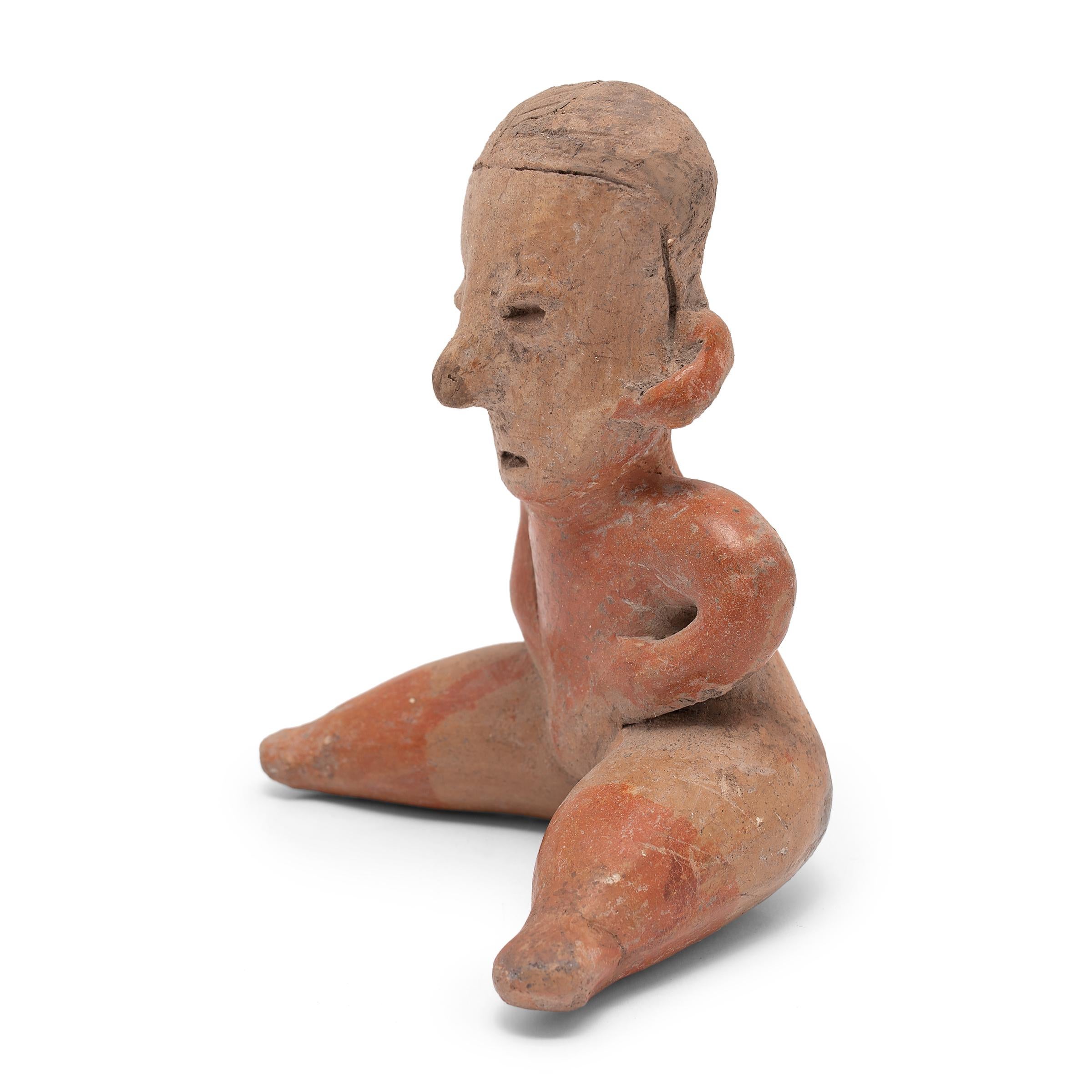 This seated effigy figure was crafted in 300 BC to 300 AD from the ancient Nayarit region of Mexico and was likely used as a ritual or burial offering. The ceramic works of the Chinesco style are often distinguished by puffy, slit-like eyes blended