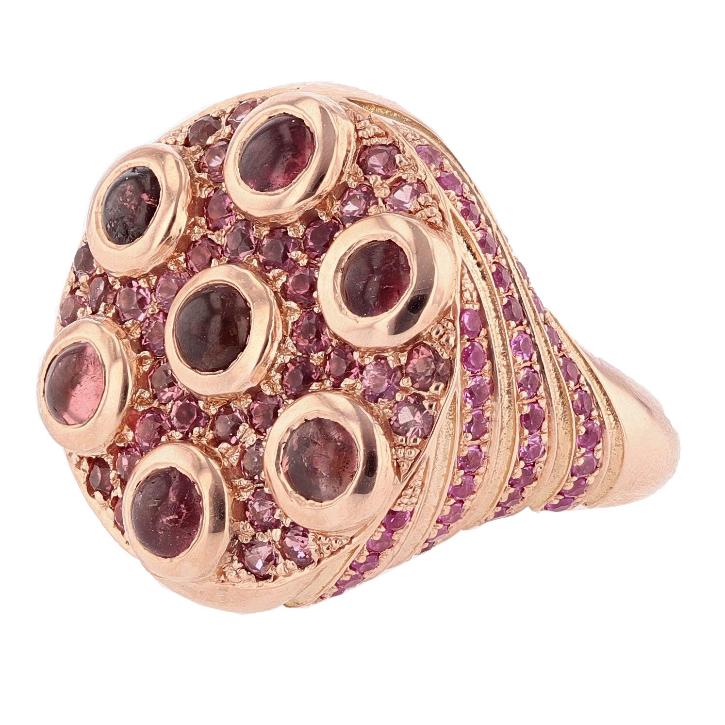This ring is designed by Nazarelle and made in 14k rose gold. The ring features 7 round cut bezel set cabochon pink tourmalines weighing 2.29ct, 74 round cut prong set pink sapphires weighing 0.84ct, and 36 round cut prong set pink tourmalines