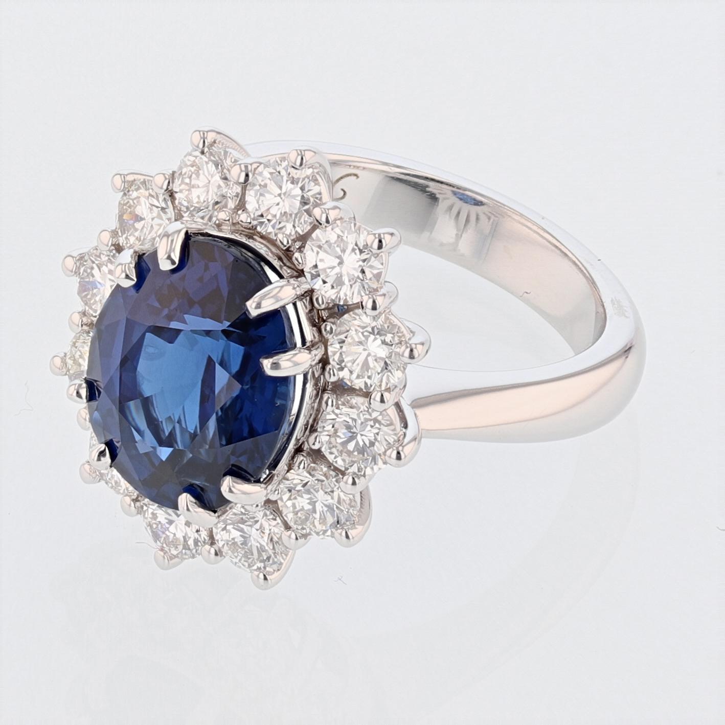 This ring is made in 18k white gold and features a GRS certified, vivid blue, oval cut sapphire weighing 6.46ct. The certificate number is GRS2015-034115. The ring also has a diamond halo featuring 12 round cut diamonds weiging 1.82ct color grade