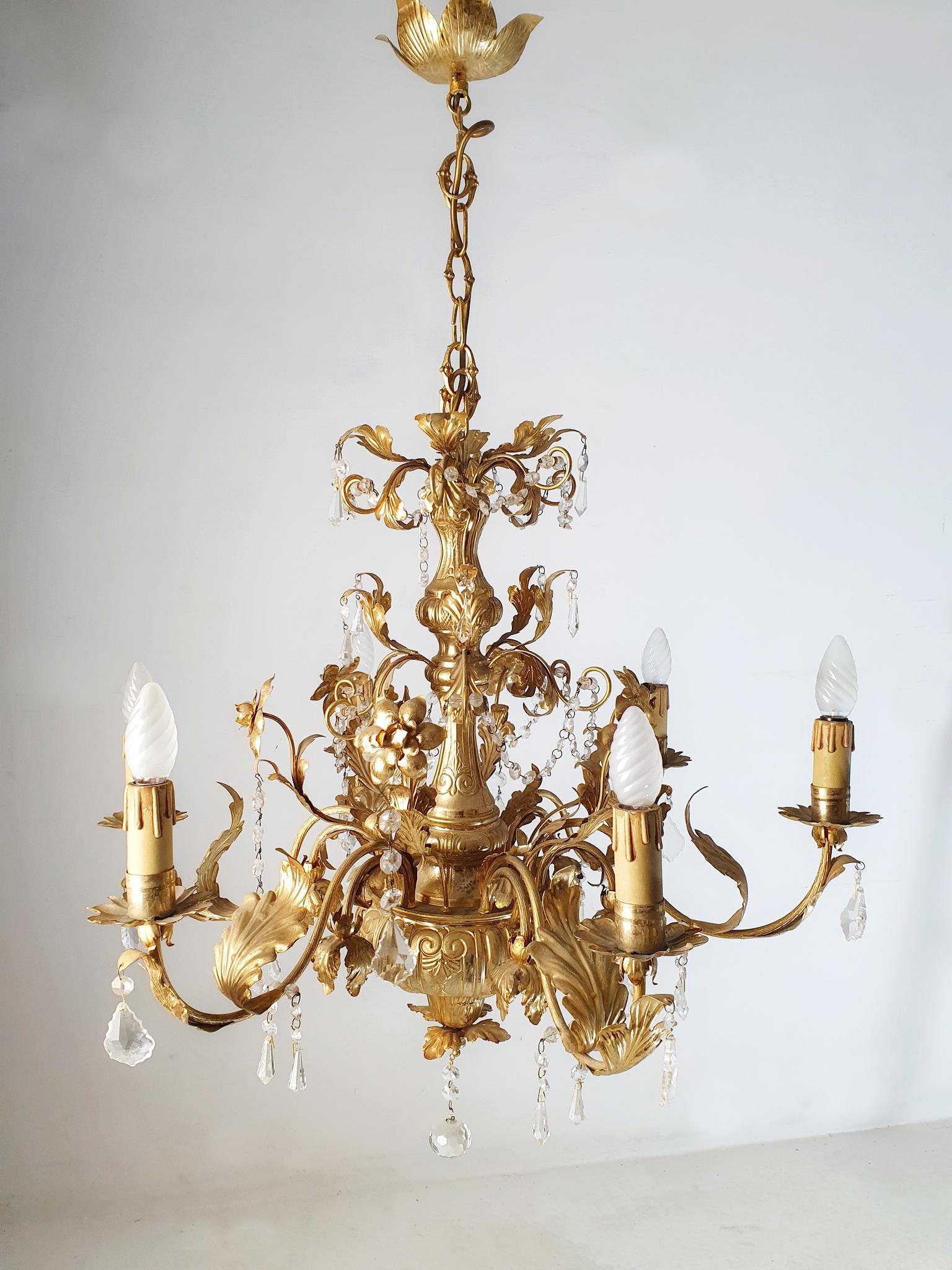 Chandelier in gold and crystal with six candle lights from the 1950's. Made from aluminium and gold plated with real gold, albeit thin, with a natural vintage patina. Ornately decorated with flowers leaves and crystals. In good working condition The